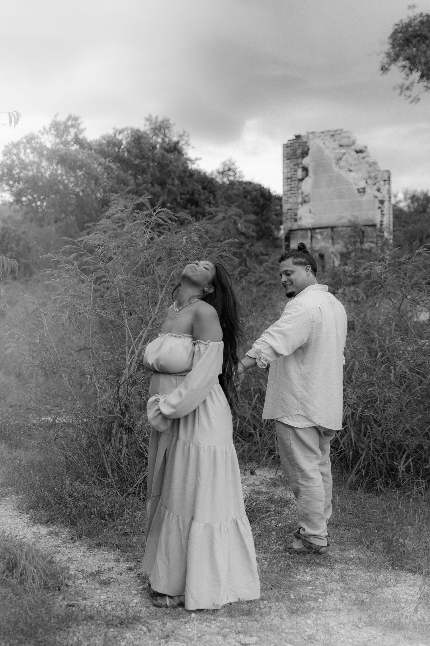 Couple in light clothing standing near old stone ruins in black and white.