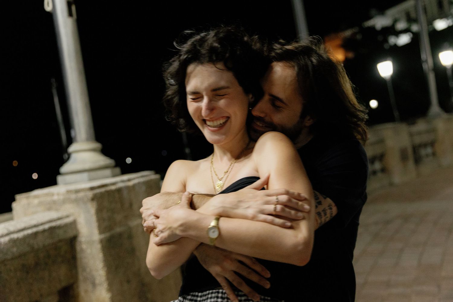 A romantic couple embraces and dances together in a dimly lit outdoor setting at night.