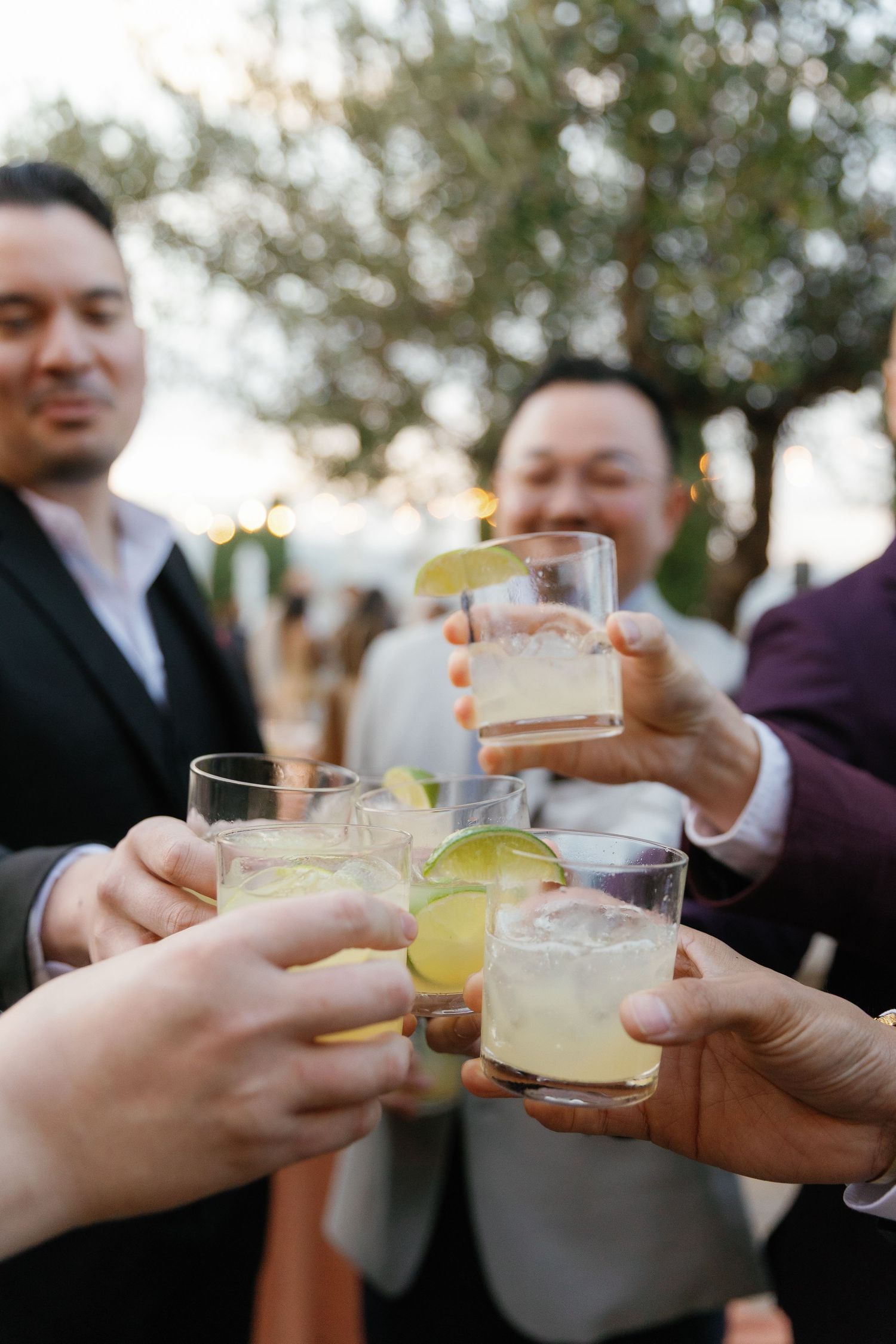 Wedding guests raise glasses in a celebratory toast with citrus cocktails at an outdoor reception.