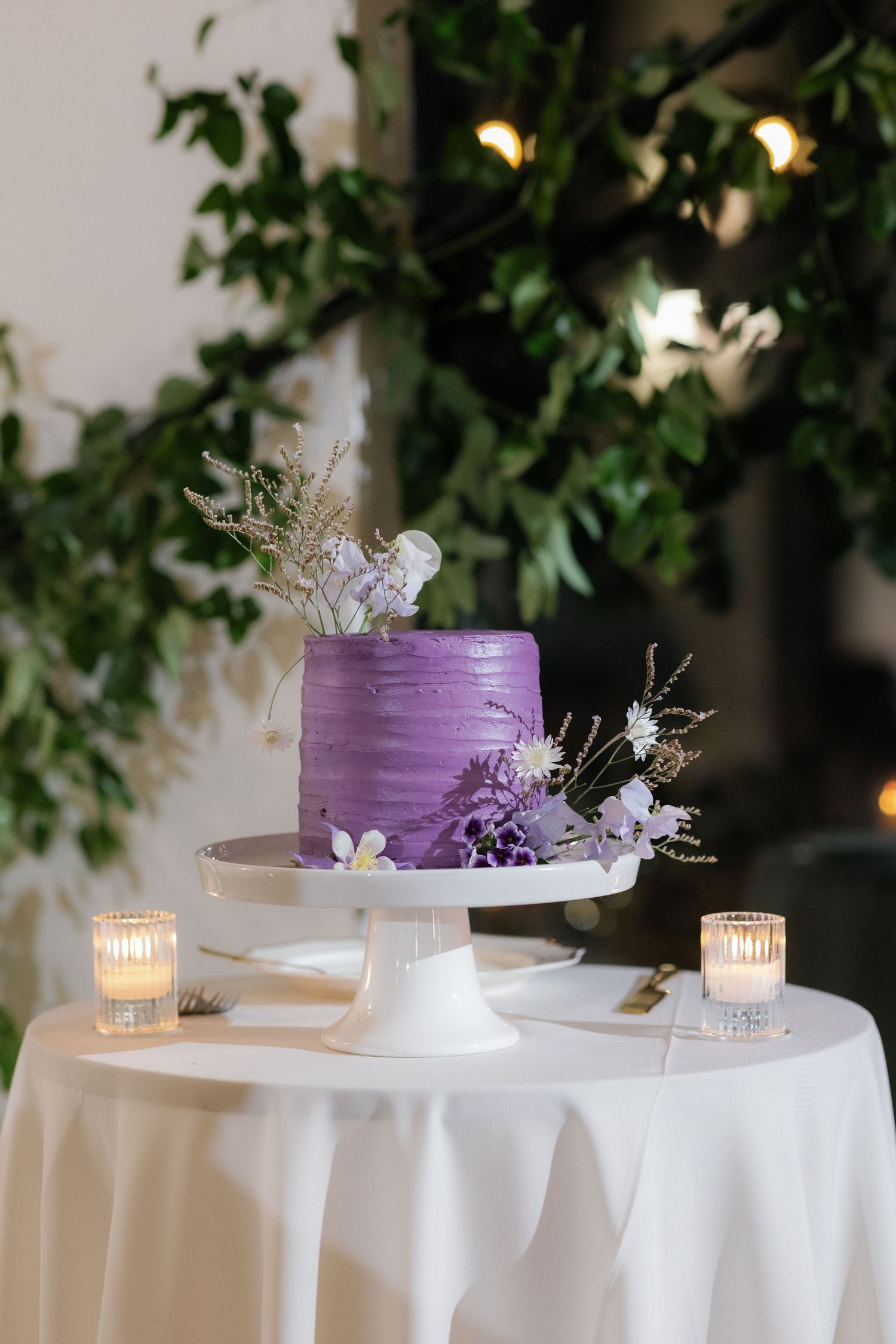 Purple ombre wedding cake displayed on white tablecloth with delicate floral decorations and candlelight.