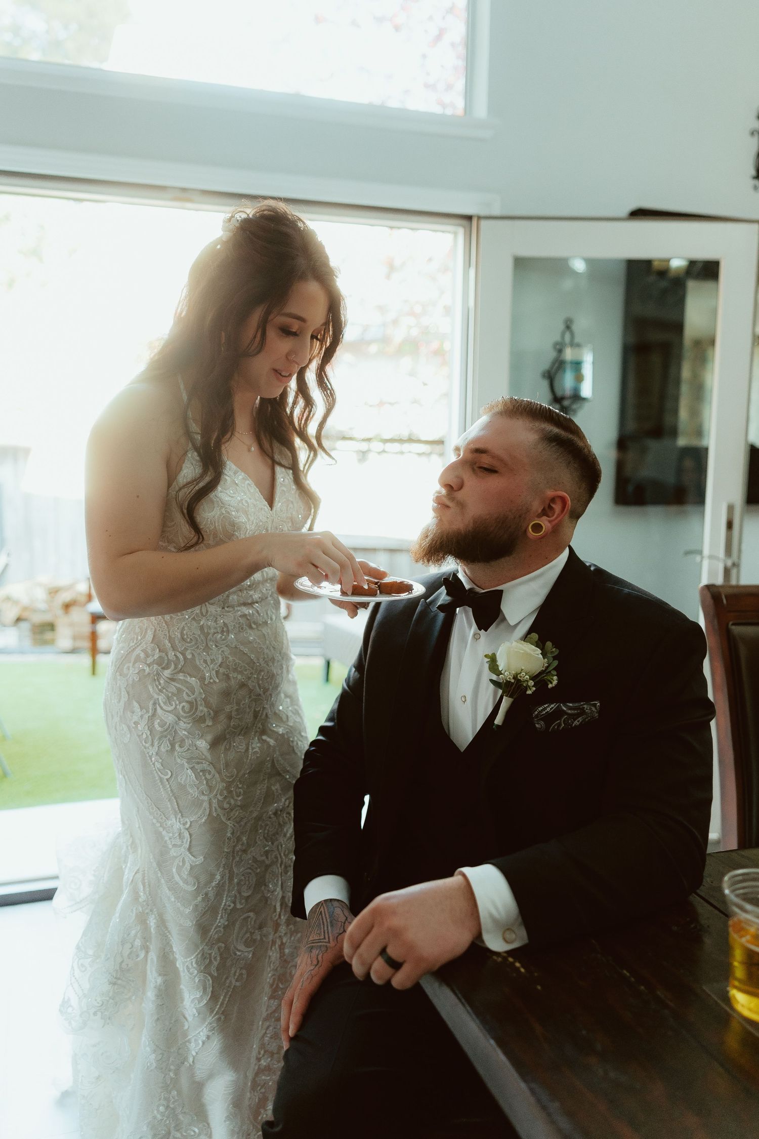 A couple shares a playful moment during their wedding as the bride feeds cake to the groom in a bright indoor setting.