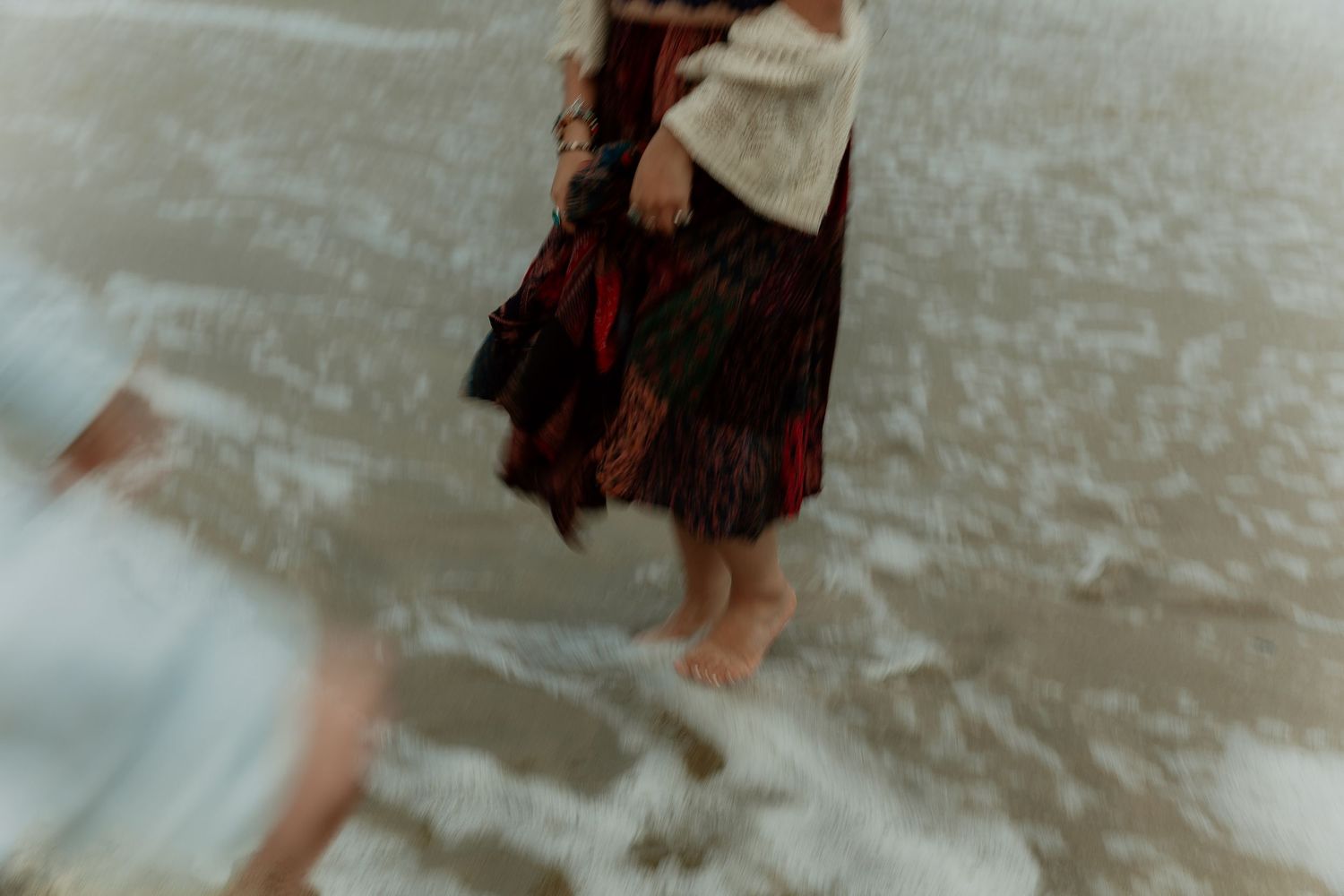 Blurred motion shot of legs walking at a beach shoreline with water washing over feet.