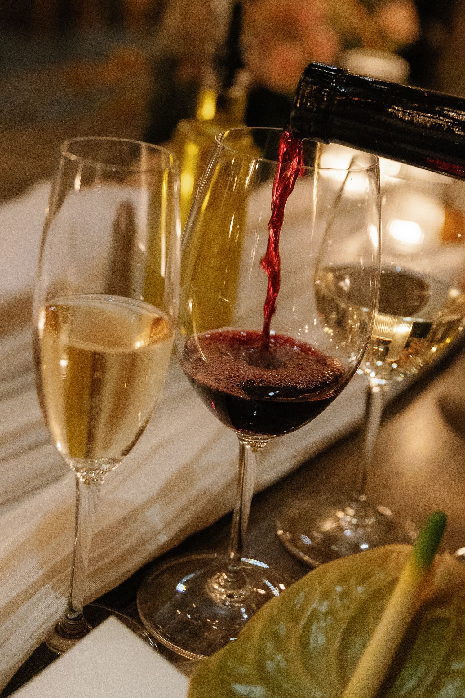 Red wine being poured into a glass next to champagne flutes on an elegant dining table setting.