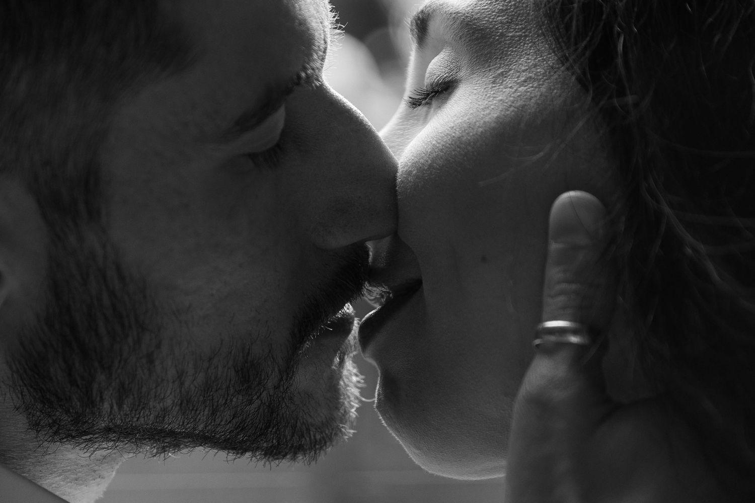 A romantic black and white photograph of a couple sharing an intimate kiss in dramatic lighting.