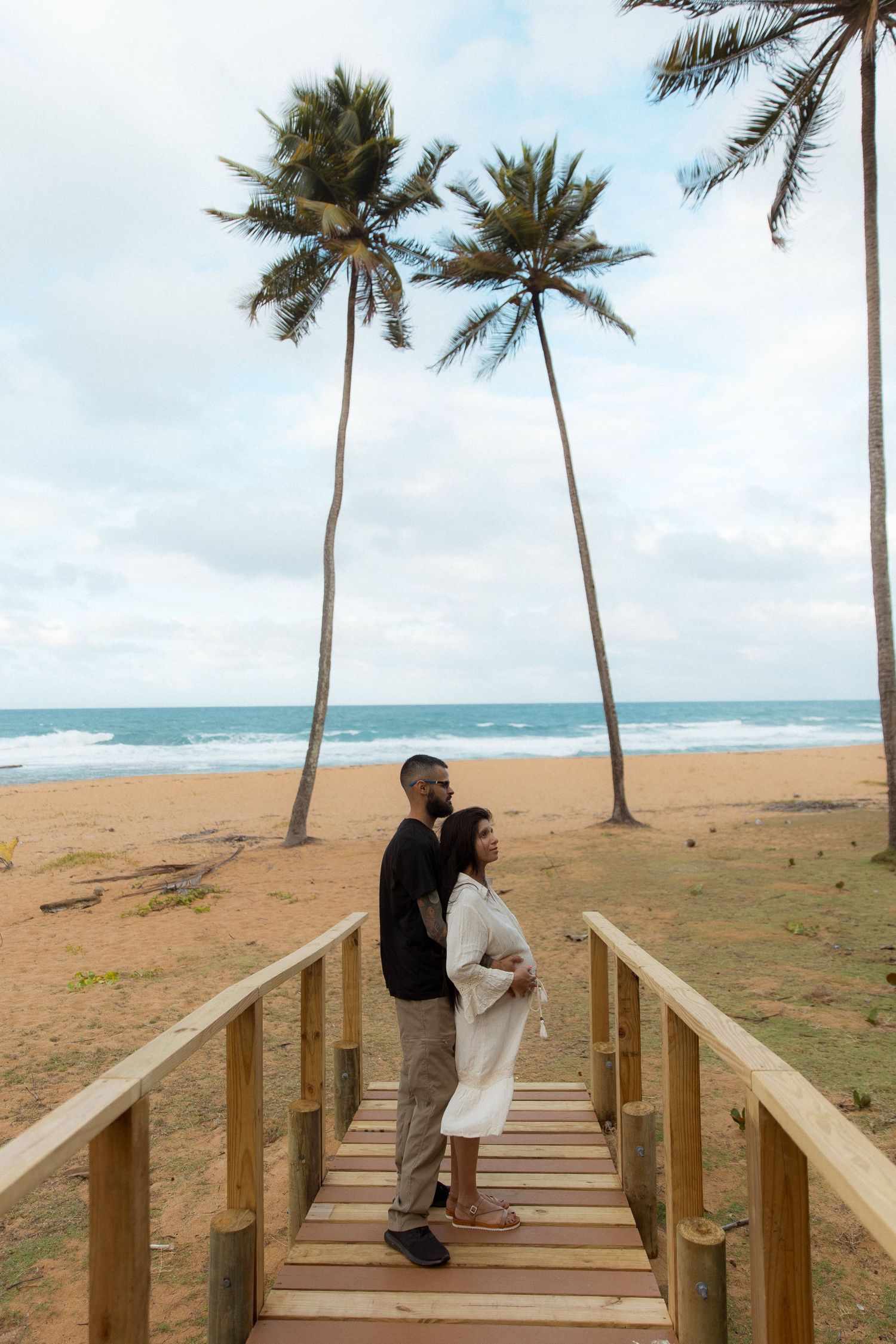 A wooden boardwalk leads to a tropical beach with palm trees and turquoise ocean waters of Piñones, Puerto Rico in the background.