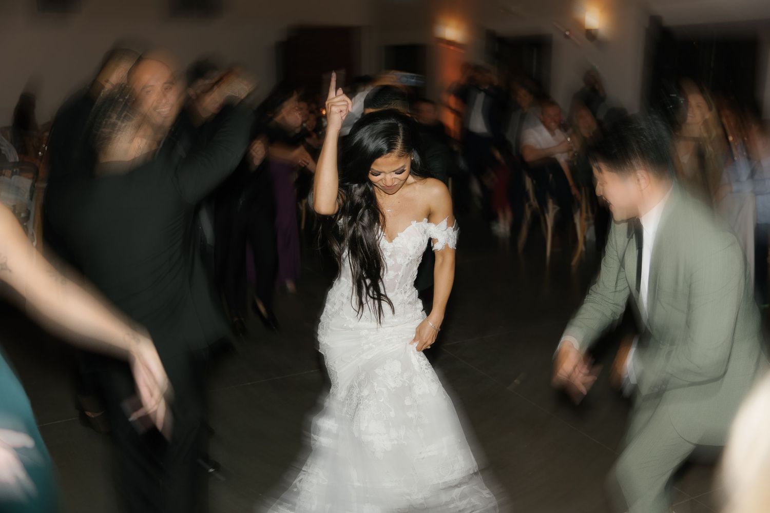 A couple shares their first dance at a wedding reception surrounded by guests on a dimly lit dance floor.
