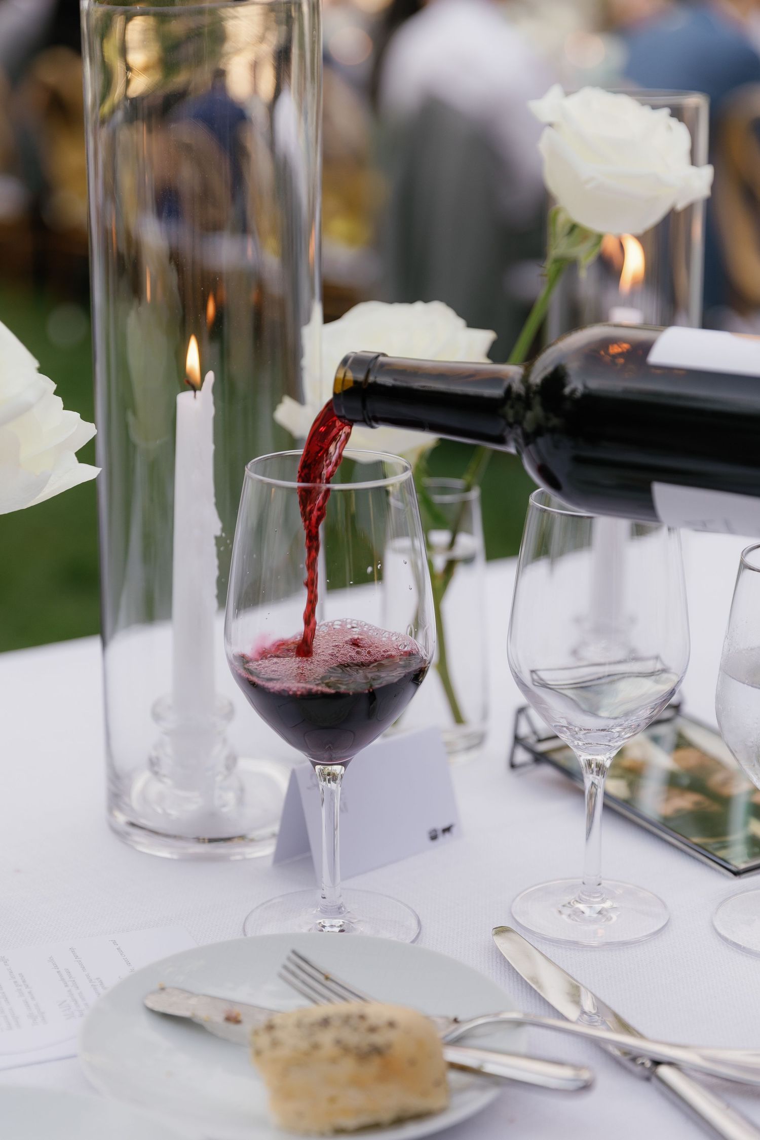 Wine being poured into glasses at an elegant table setting with white linens and glass stemware.