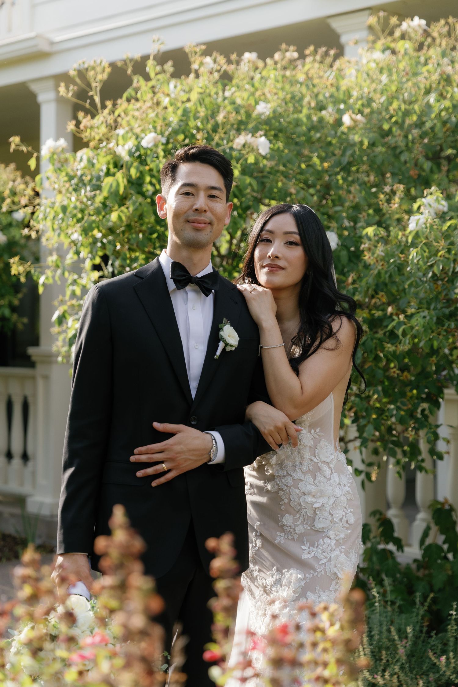 A bride and groom share joyful moments in a garden setting with blooming flowers and greenery.
