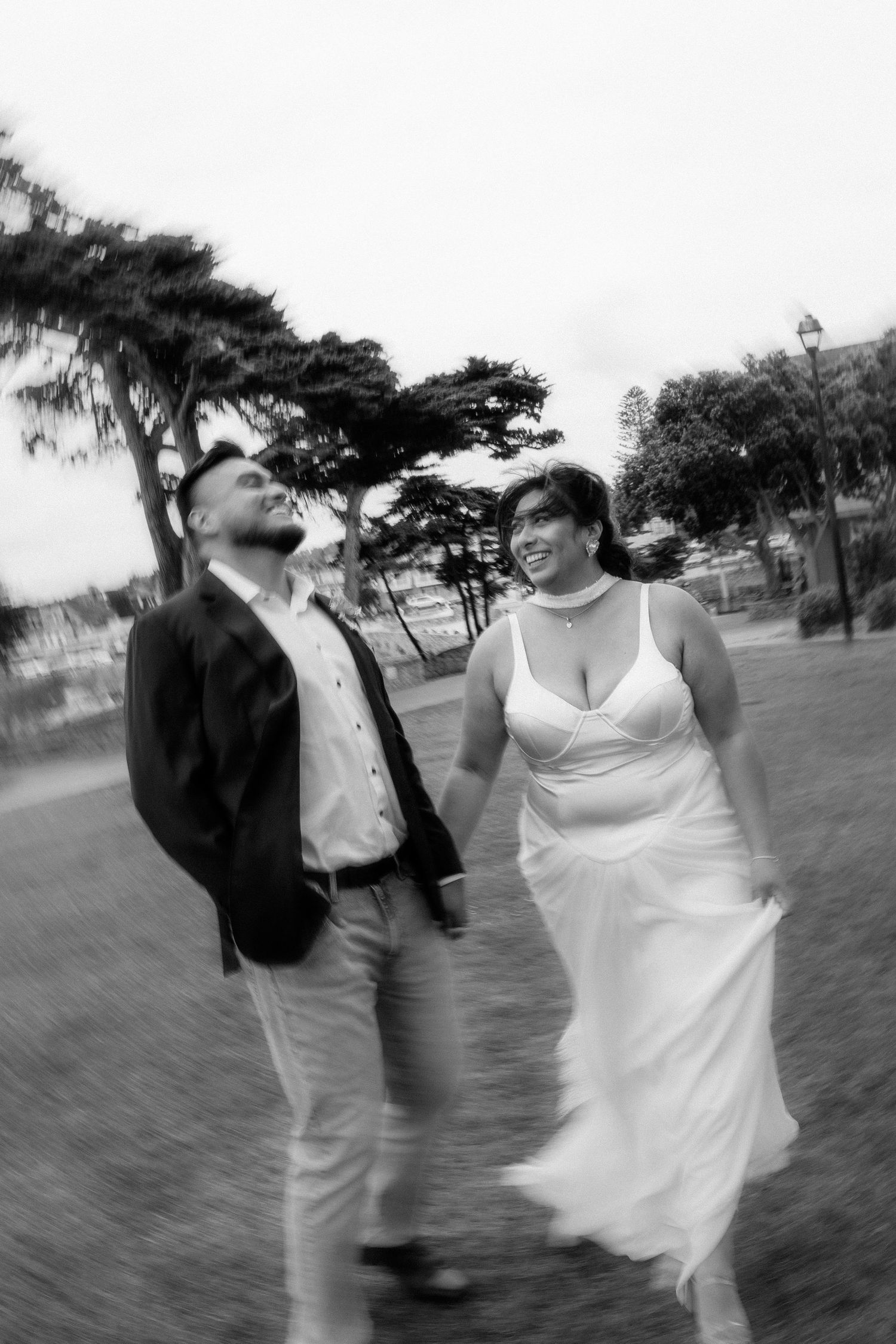 A candid black and white photo of two people walking and laughing together in a park setting.