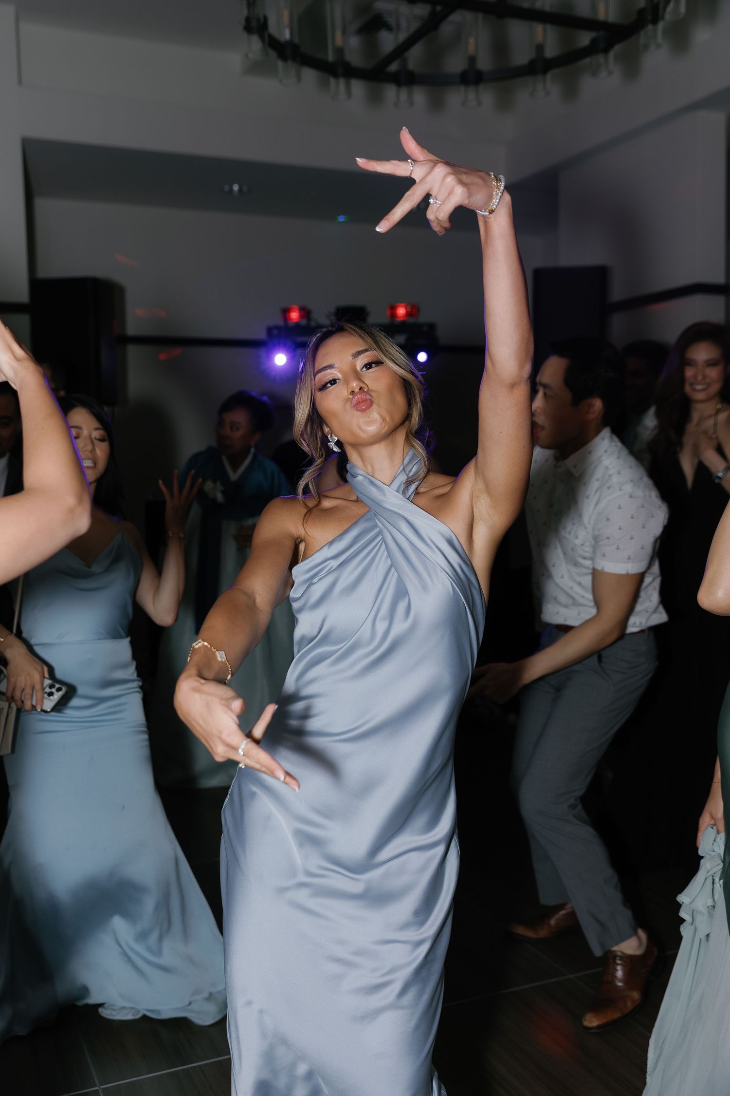 Wedding guests dancing energetically in light blue dresses at a dimly lit reception party.