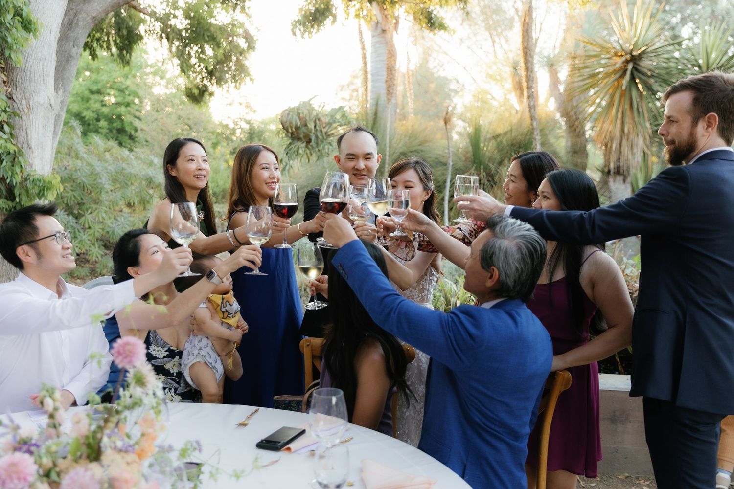 Wedding guests raising glasses in a sunset toast during an outdoor reception celebration.