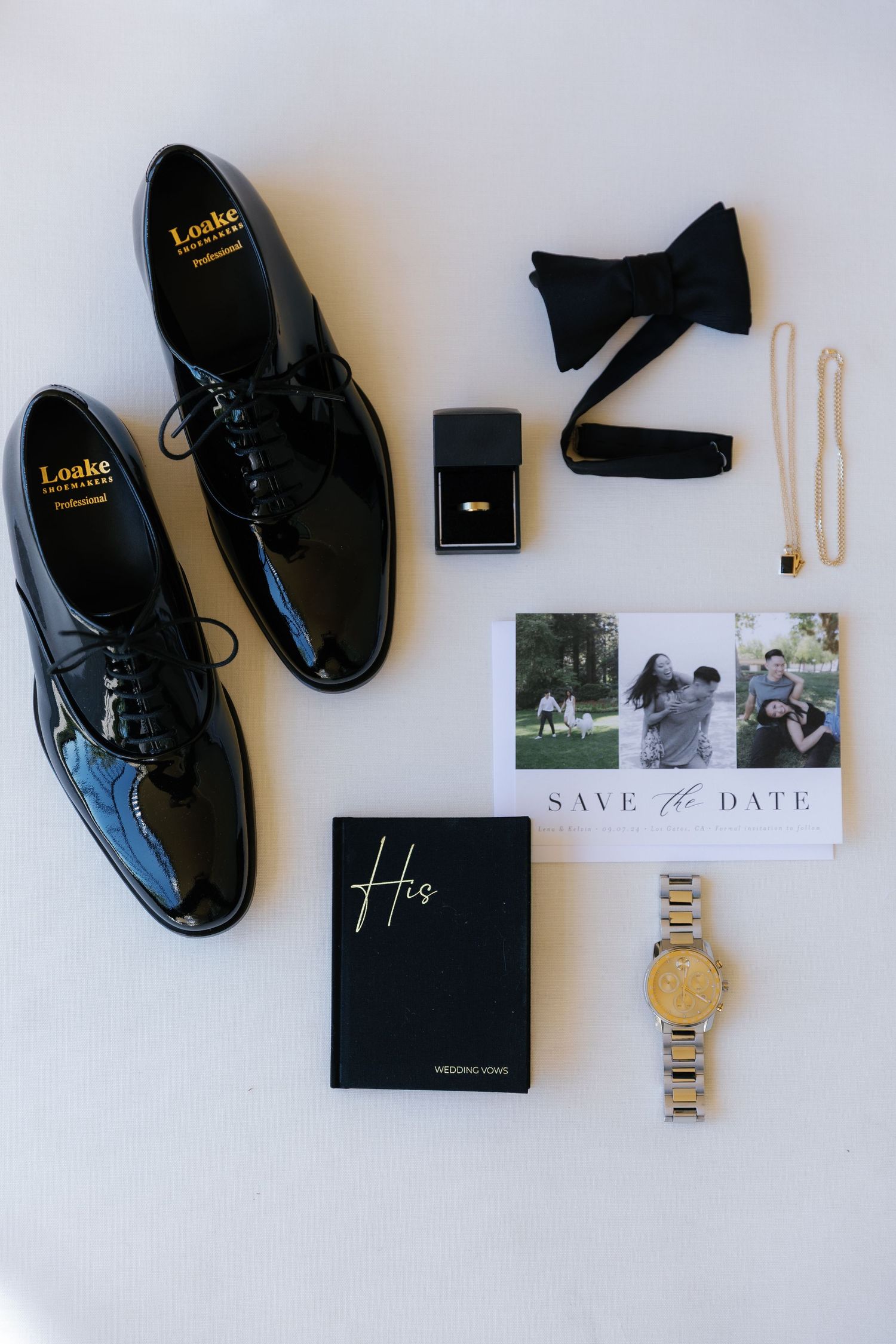 Wedding accessories flatlay with black dress shoes, bow tie, watch, and save the date cards.