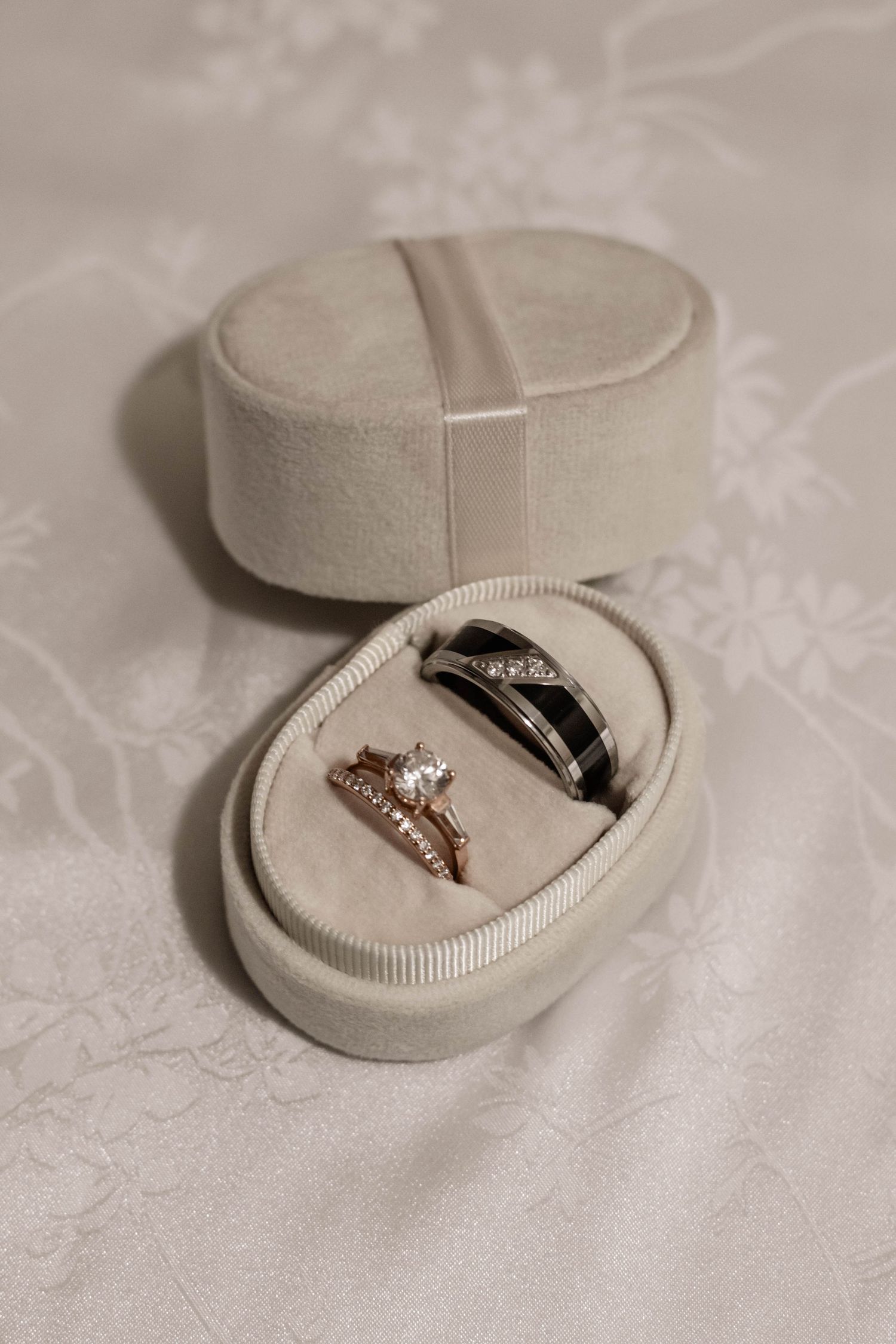 Elegant wedding ring set in ivory velvet box, featuring rose gold diamond engagement ring and black band with diamonds.