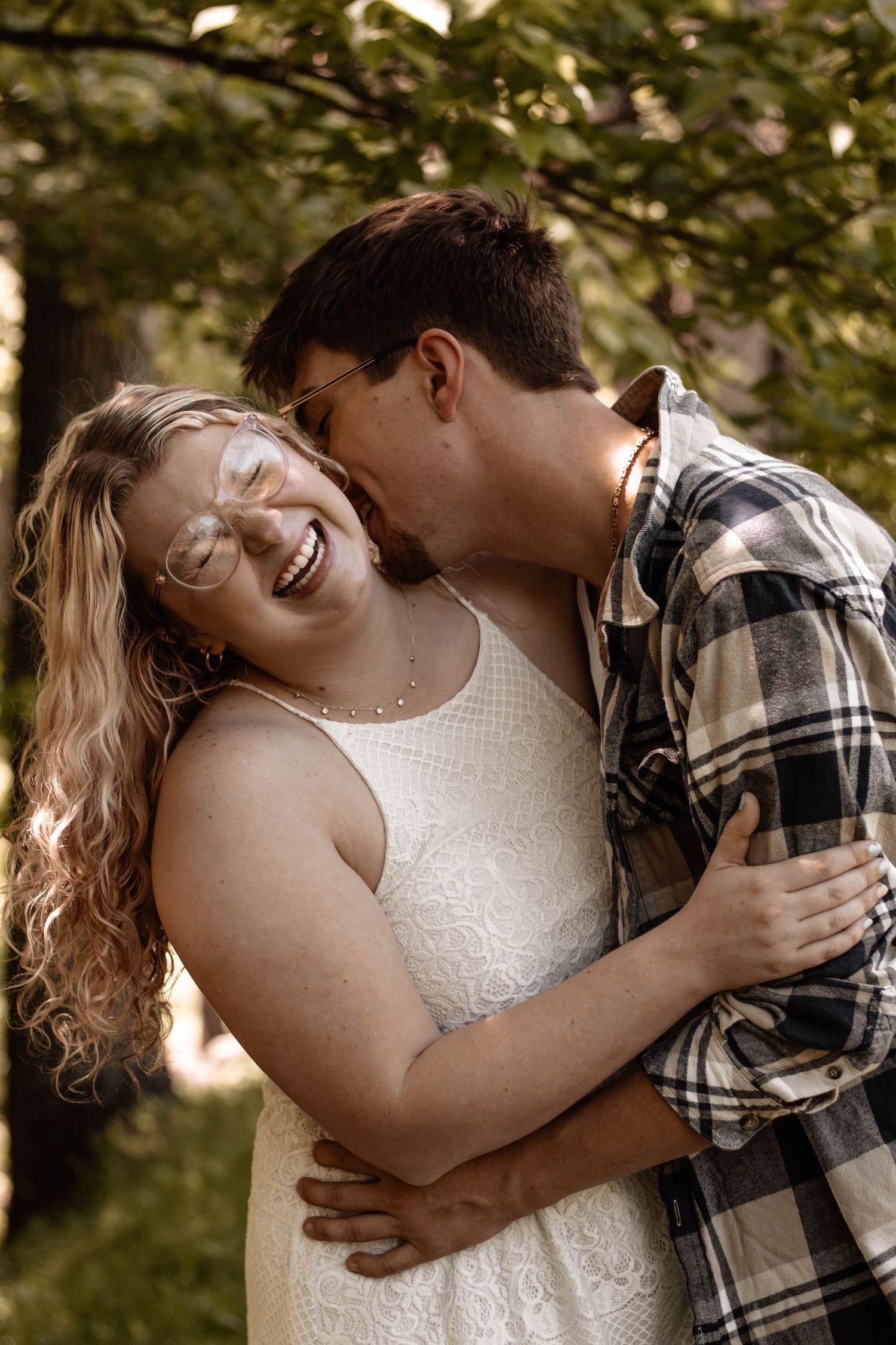 Romantic couple sharing a joyful moment outdoors, with her wearing a white dress and him in a plaid shirt.