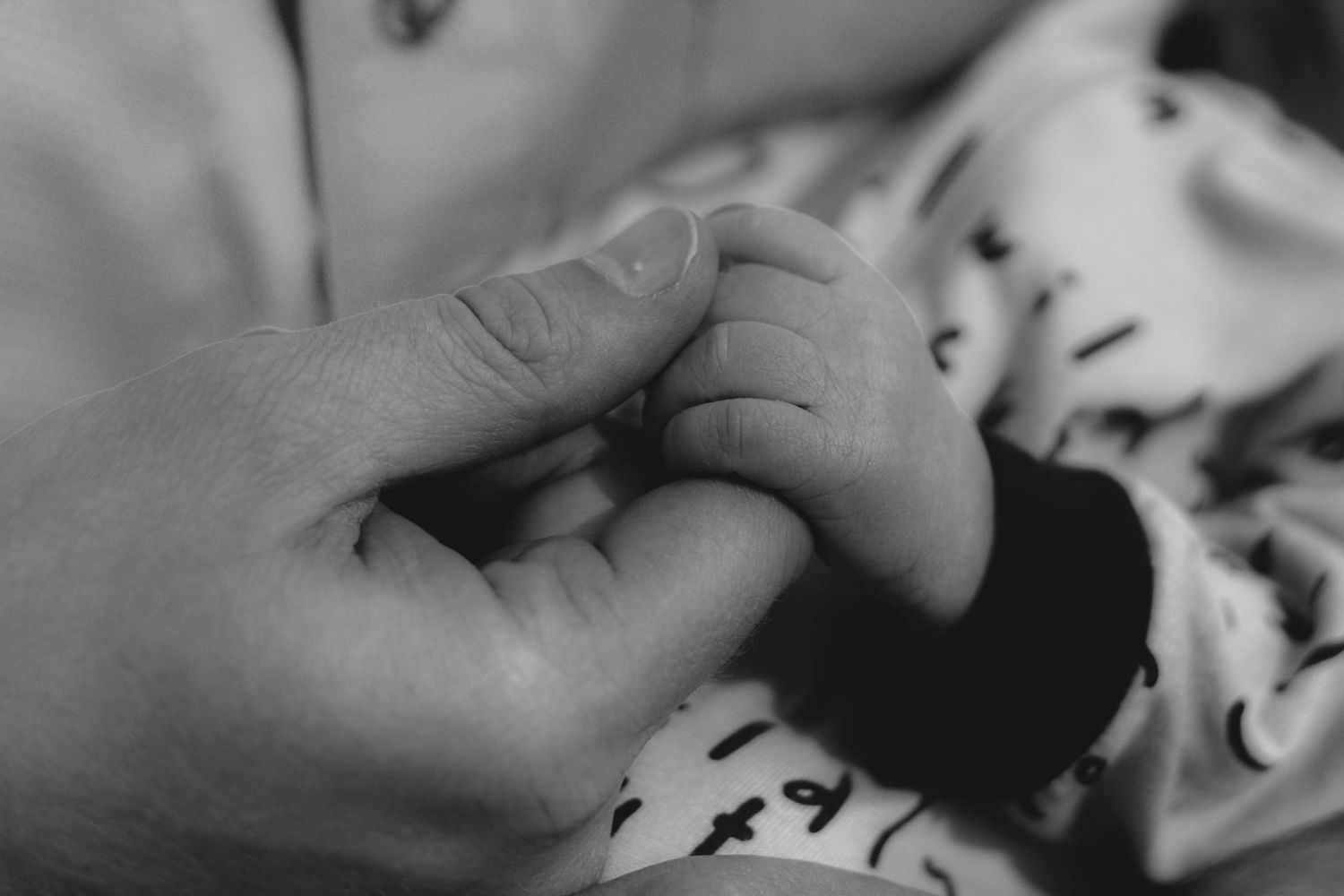 Black and white close-up of adult hand holding tiny baby foot.
