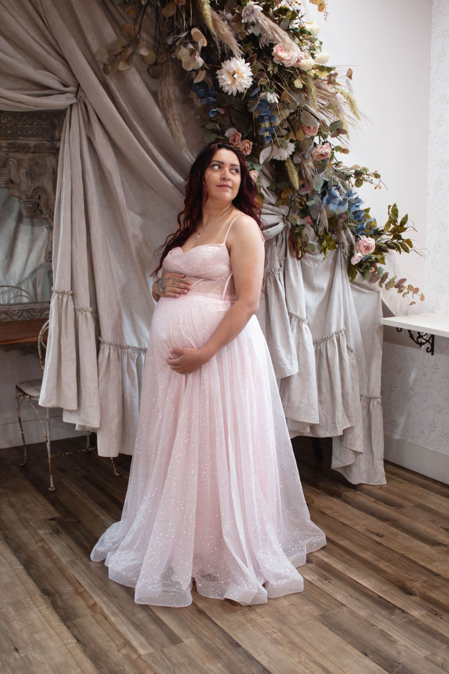 Maternity photo of woman in sparkly pink gown against floral backdrop.