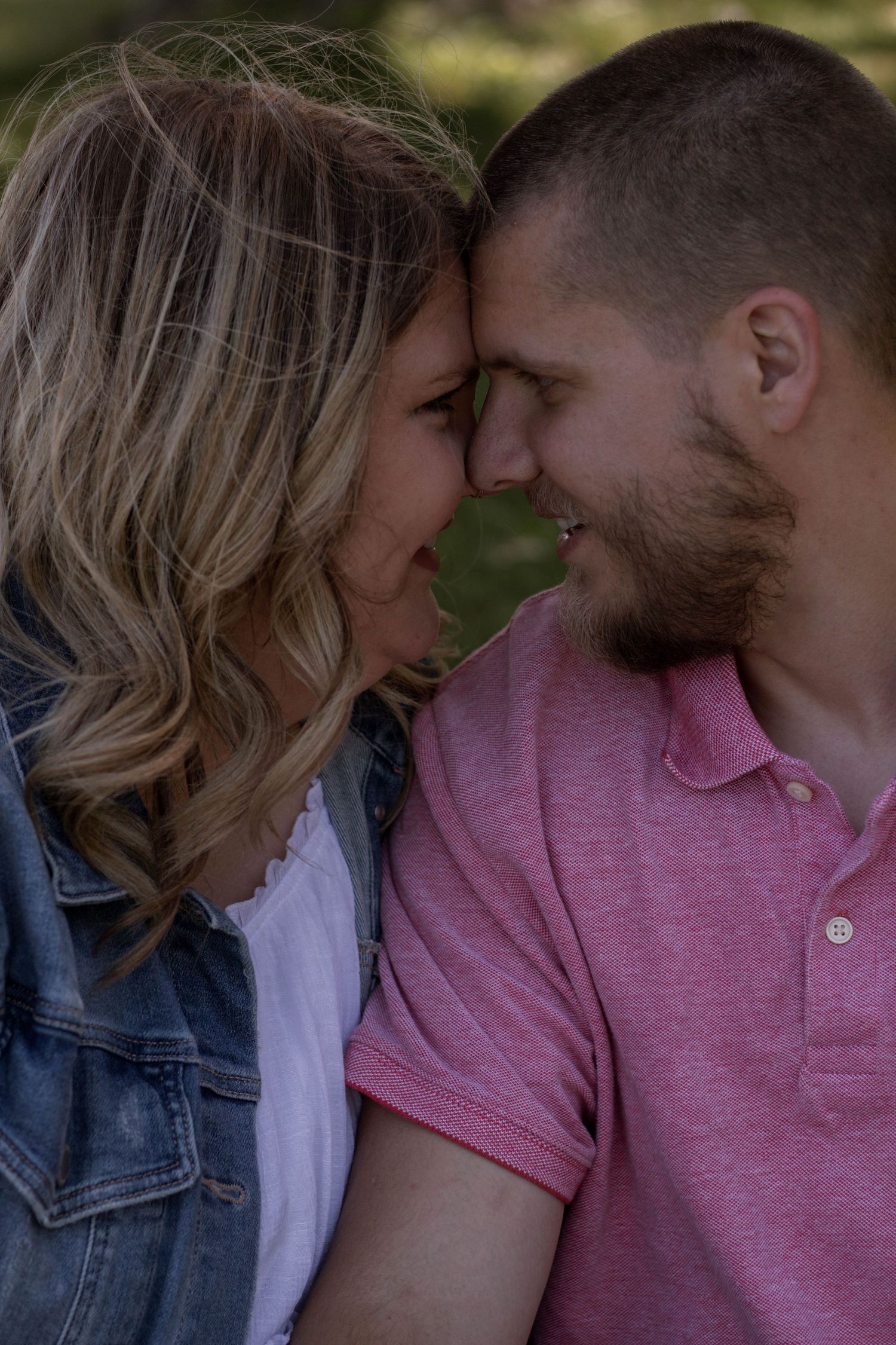 A romantic couple shares an intimate moment outdoors while wearing casual denim and pink clothing.