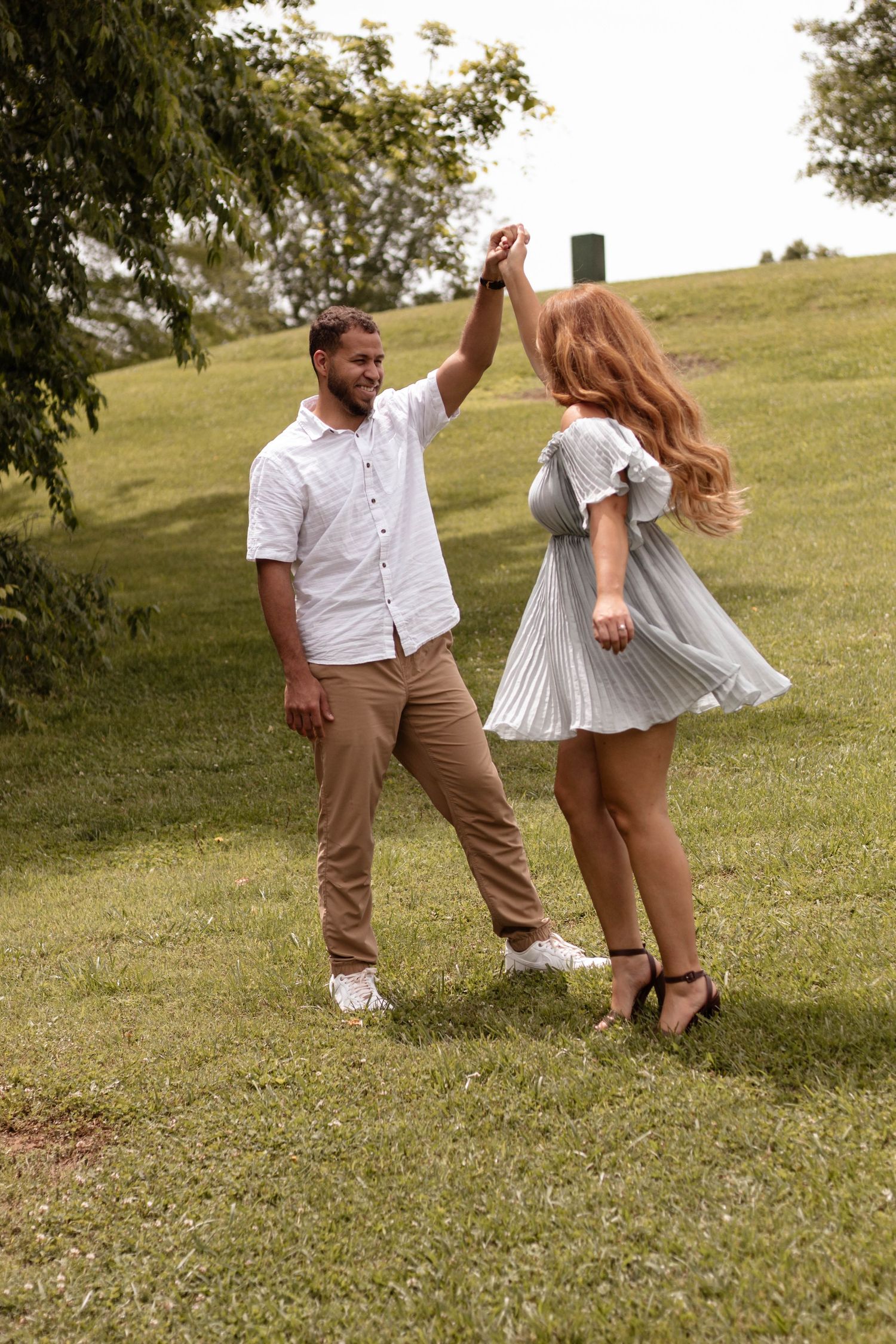 A couple dancing and twirling in a grassy field on a sunny day.
