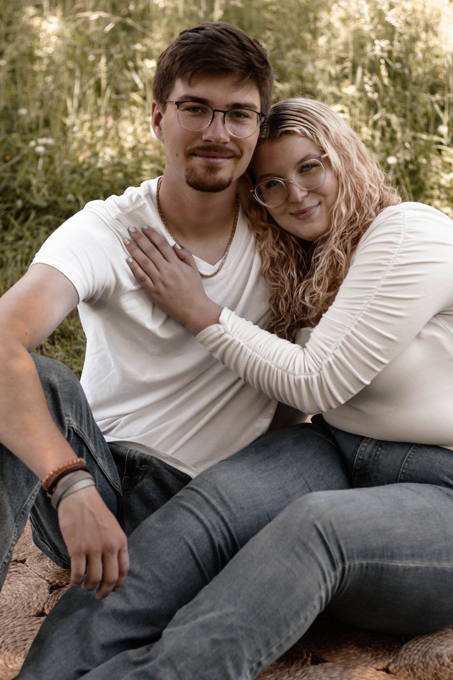 Couple sitting close together outdoors with golden sunlight filtering through trees behind them.