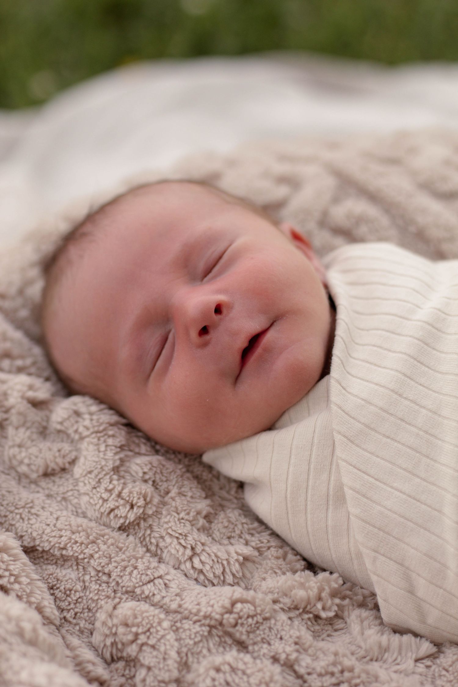 A peaceful sleeping newborn wrapped in a white blanket resting on soft beige bedding.