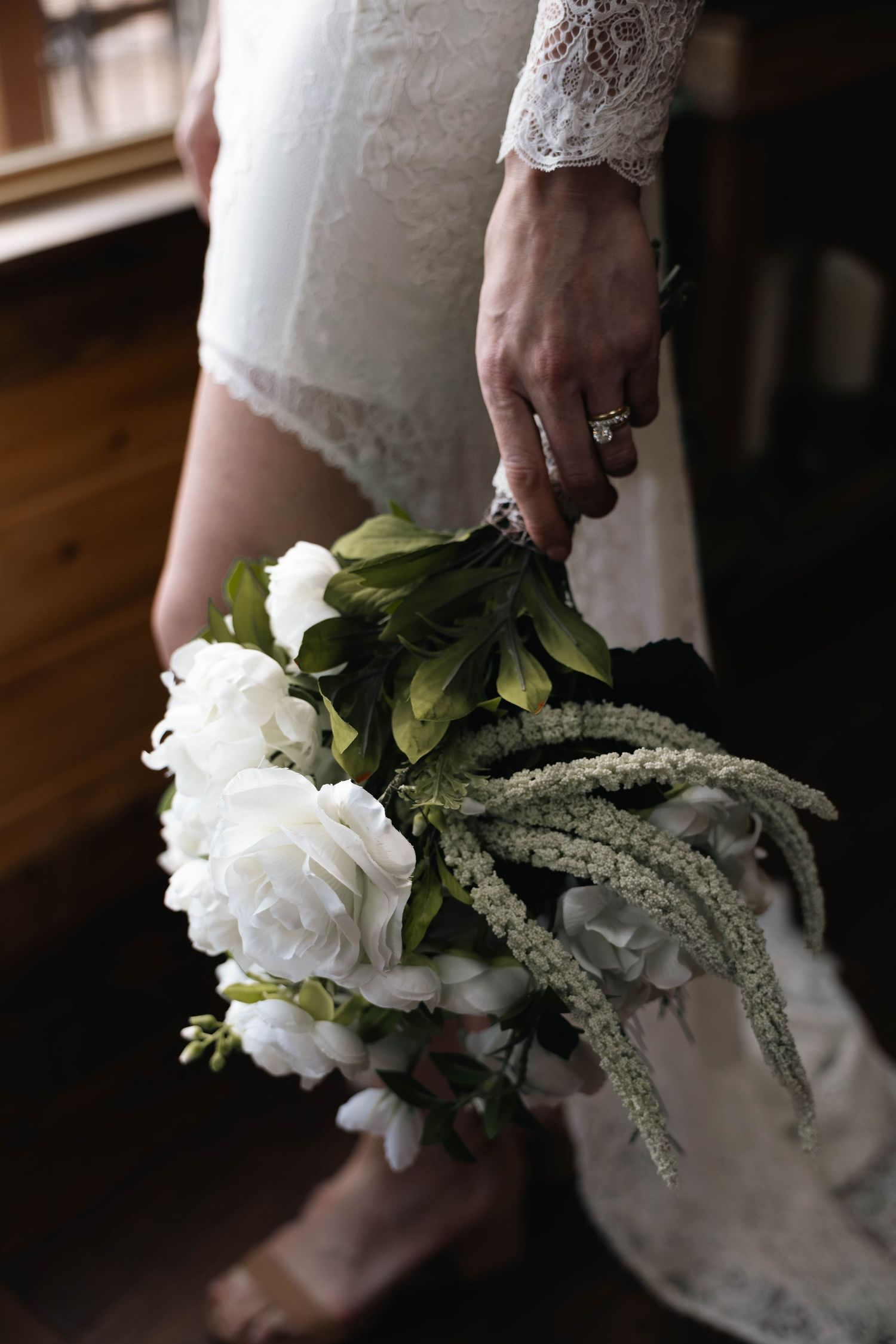 Bride in lace wedding dress holding elegant white peony bouquet with greenery and cascading amaranthus.