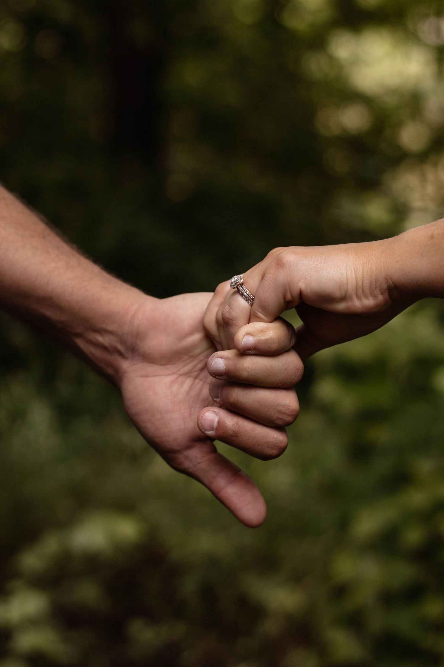 Close-up of hands holding together with engagement ring visible in natural setting.