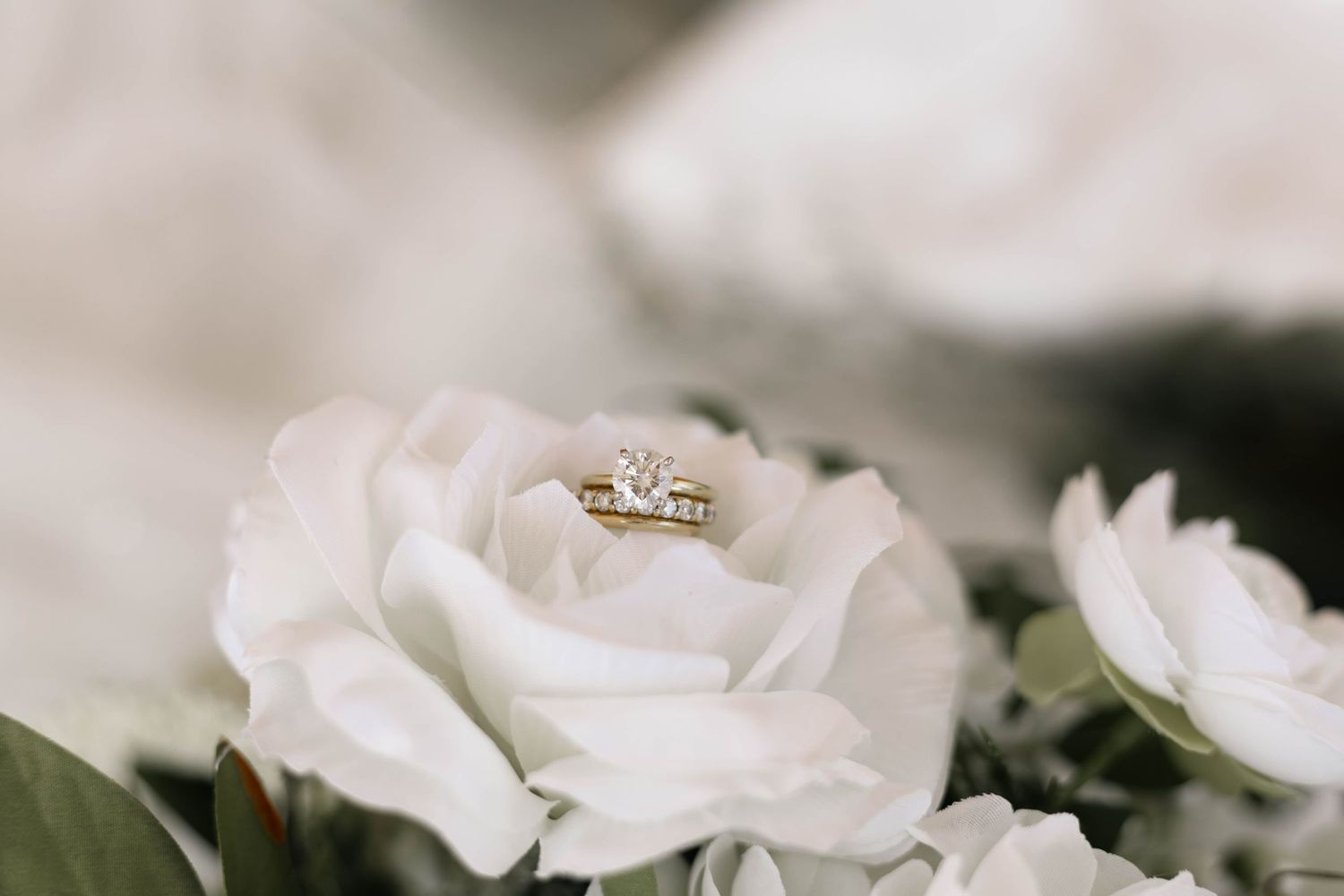 Gold diamond engagement ring resting elegantly on white roses in a bridal bouquet.