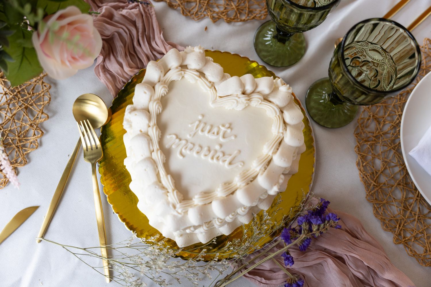 Close-up of a heart-shaped just married white wedding cake with ruffled frosting on a gold cake board.