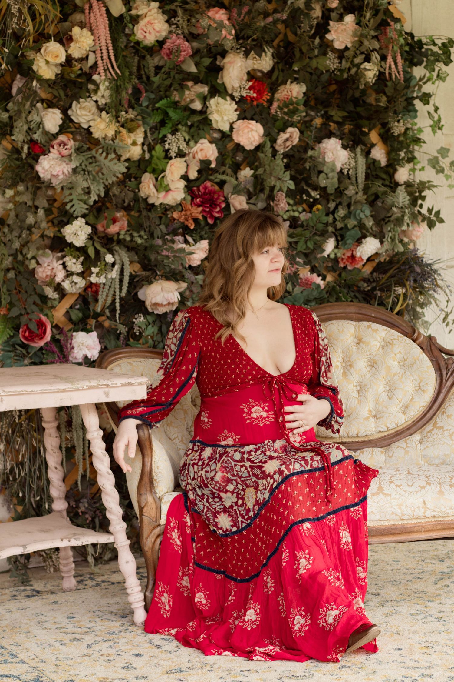 A romantic scene with roses and floral decor featuring someone in a flowing red lace dress sitting on an antique sofa.