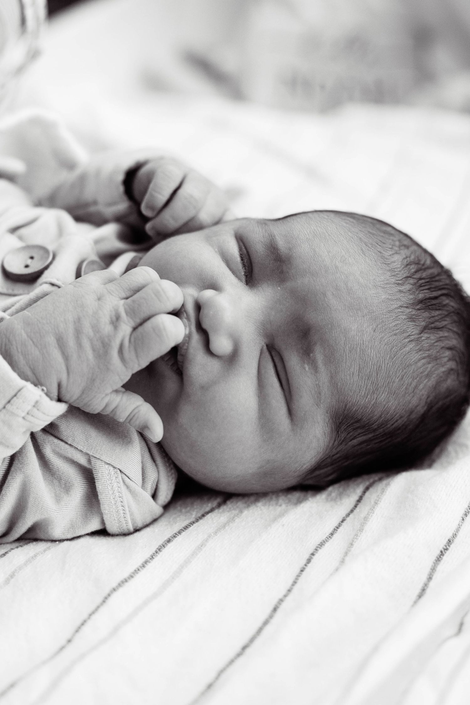 Sleeping newborn baby in gray onesie lying on white striped blanket in black and white photography.