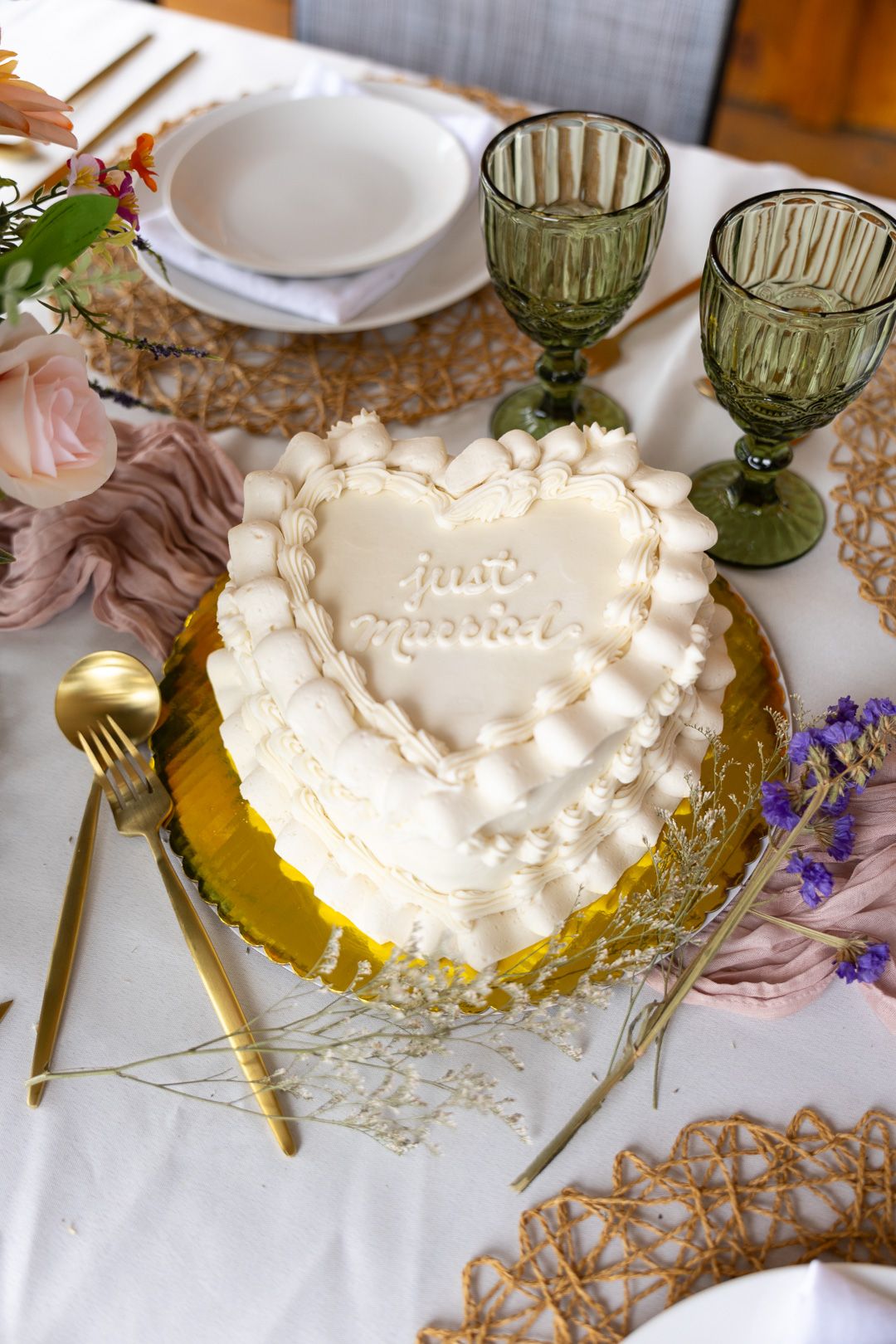 Heart-shaped white wedding cake inscribed with just married on an elegant gold-trimmed table setting.