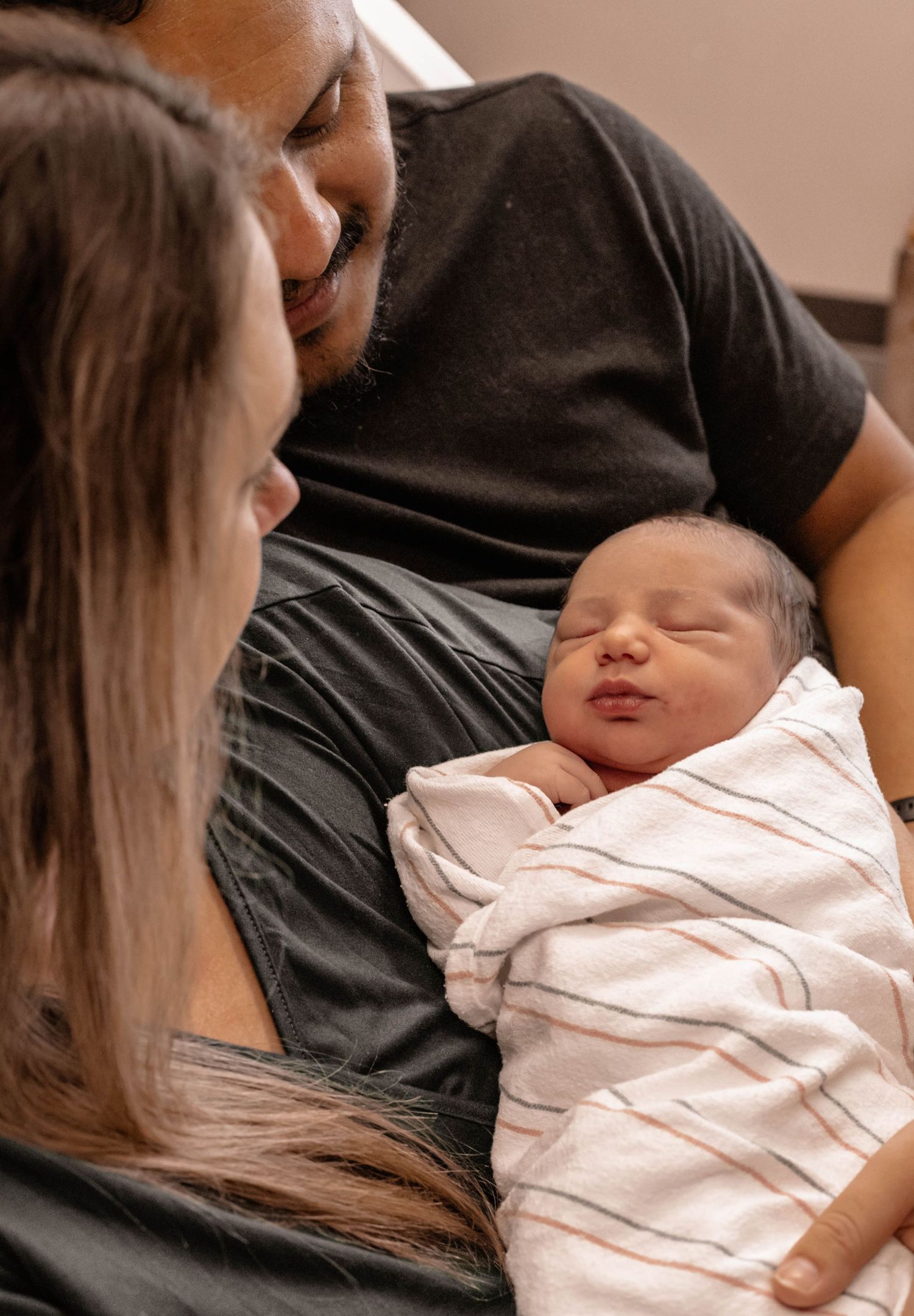 Intimate moment with newborn baby wrapped in white blanket.
