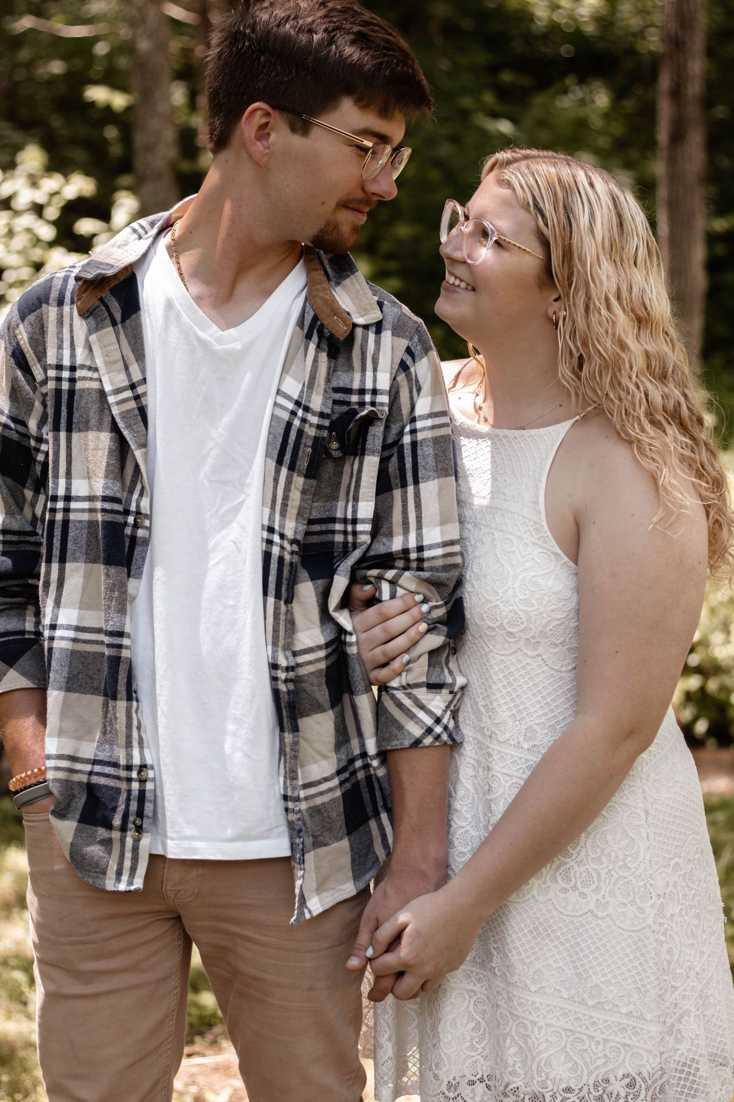 Couple in casual attire sharing loving glances while standing together in a wooded setting.