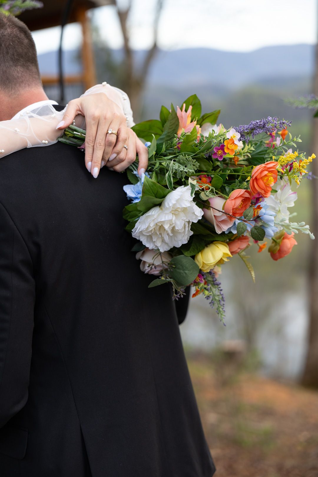 Bride holds a vibrant mixed bouquet of orange, white, and blue flowers while embracing the groom.