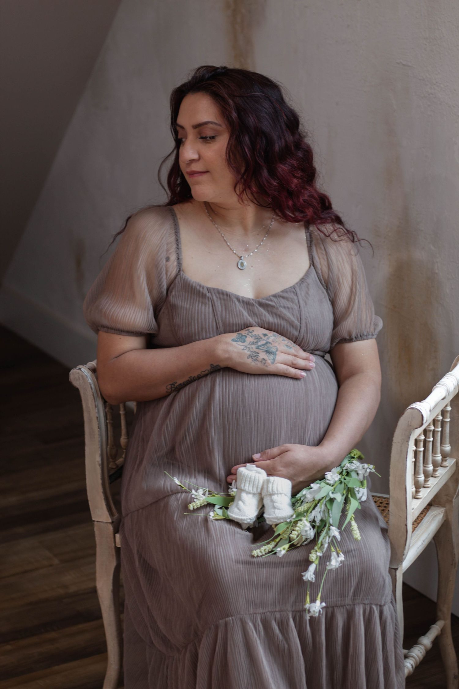 Maternity portrait of woman in flowing brown dress holding baby booties and flowers.