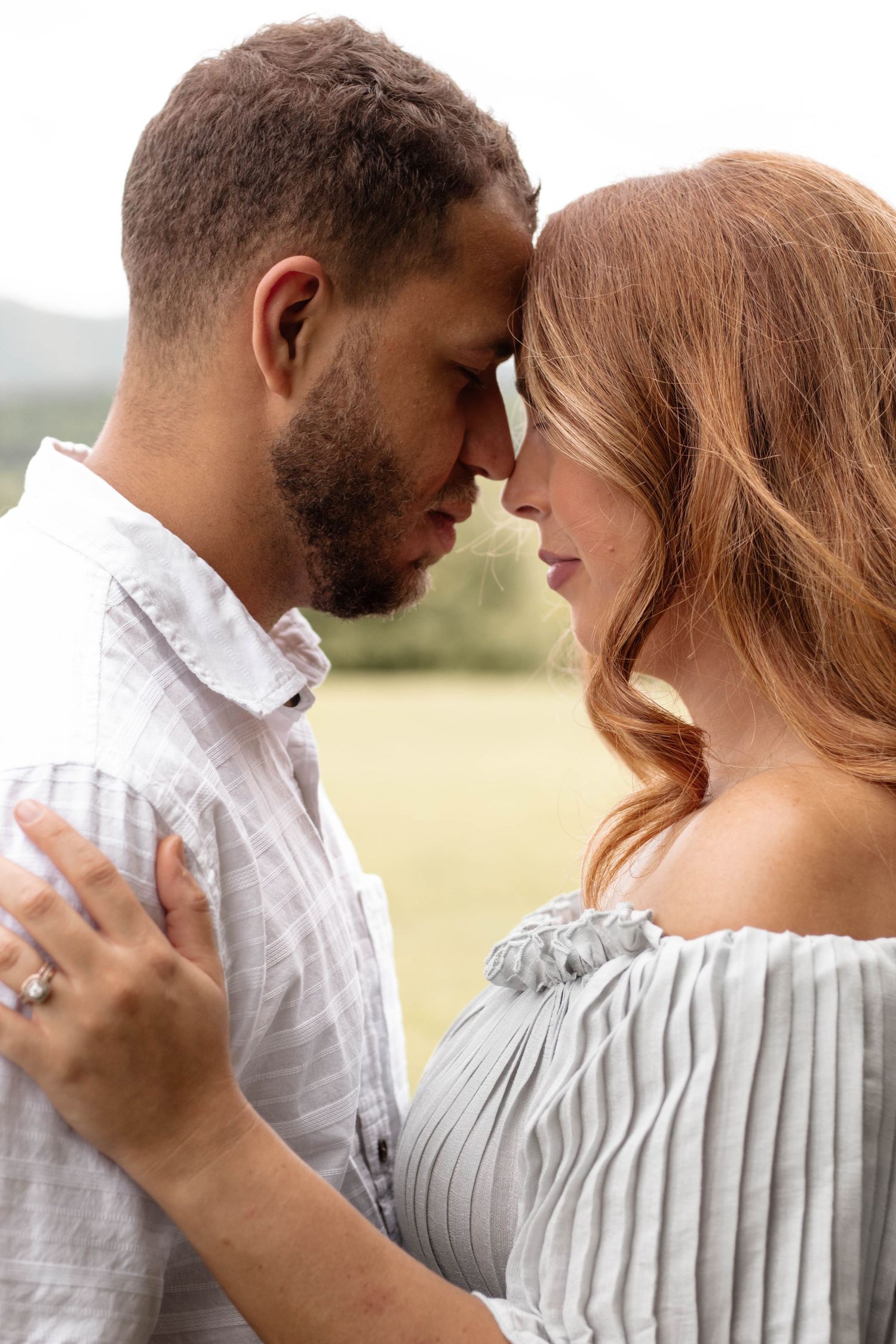 An intimate moment between a couple in white and gray attire against a rural backdrop.