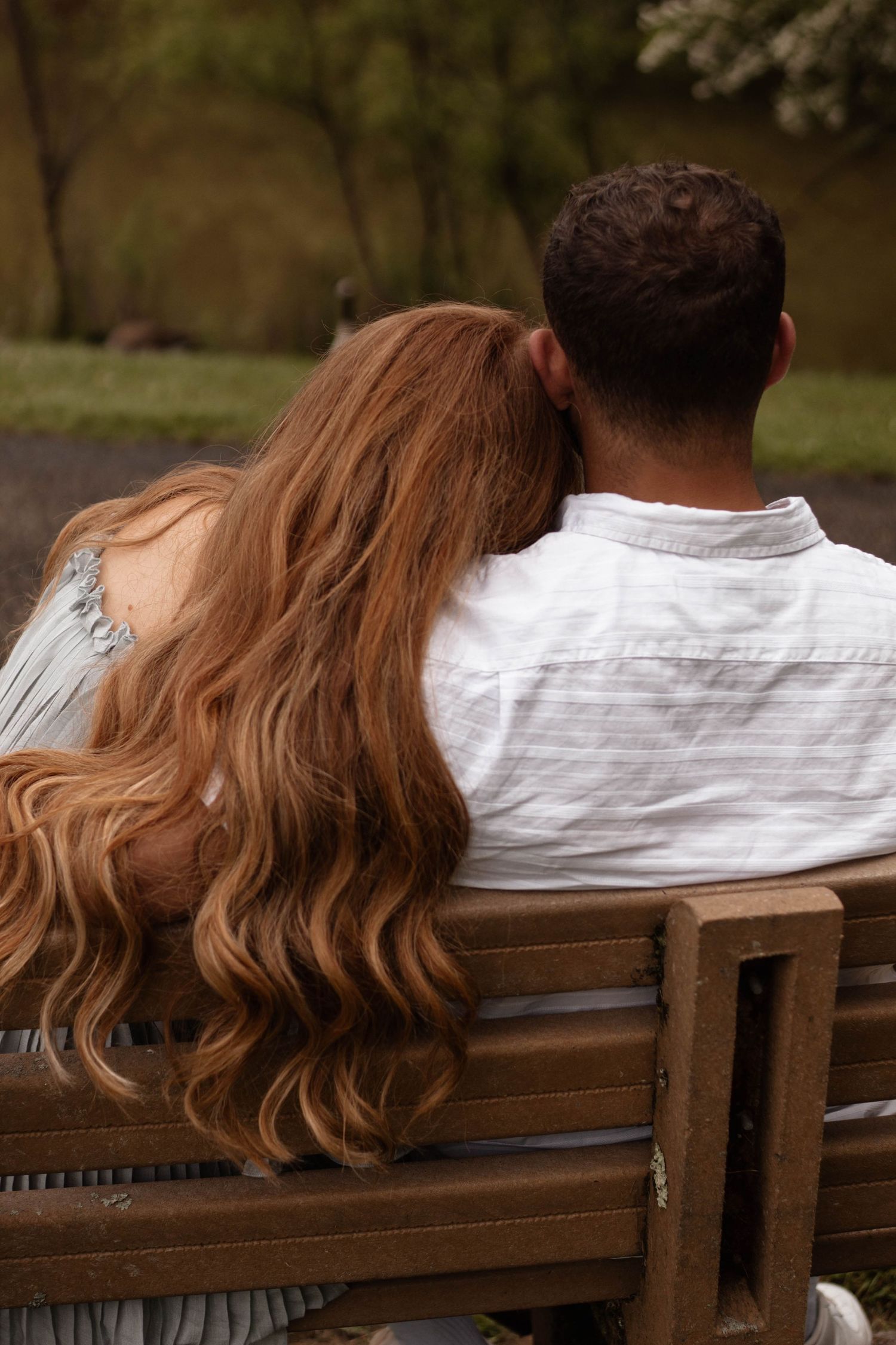 Back view of couple sitting on wooden bench with long wavy hair cascading down.