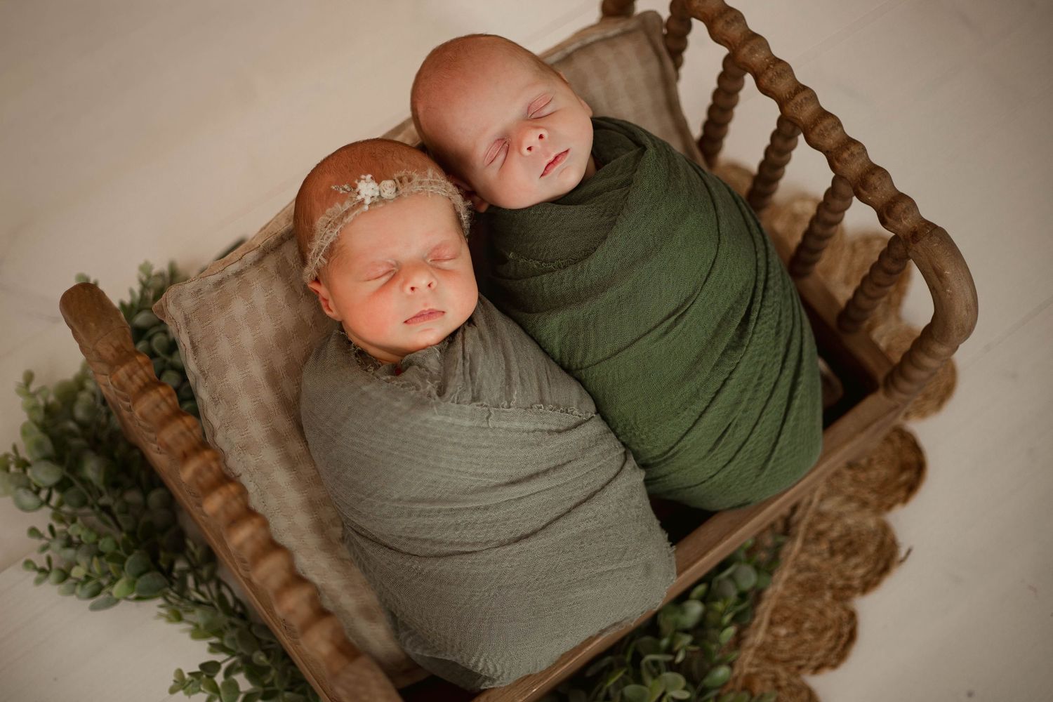 A series of newborn photography shots showing a baby wrapped in green and gray swaddles on wooden props with greenery.