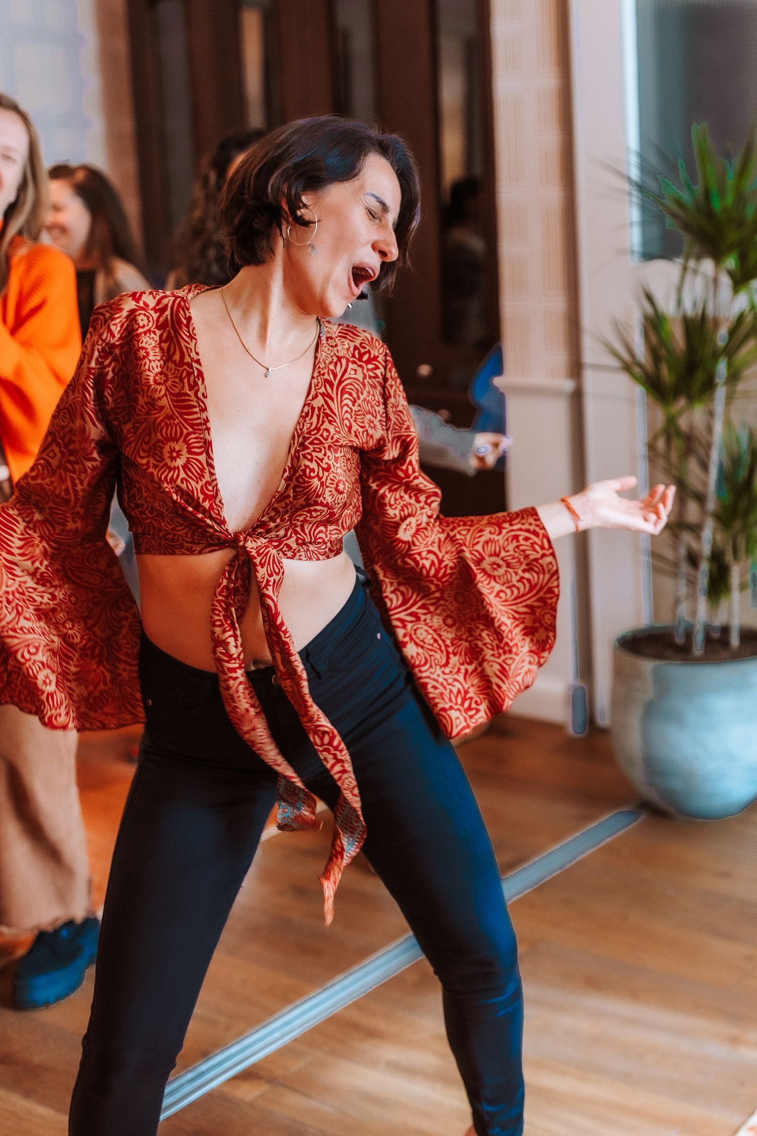 Woman in red patterned crop top and black pants dancing energetically indoors at a social event.