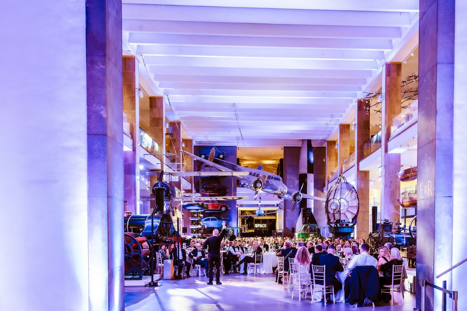 Elegant event venue with purple lighting, tall columns, and guests dining in a grand hall.