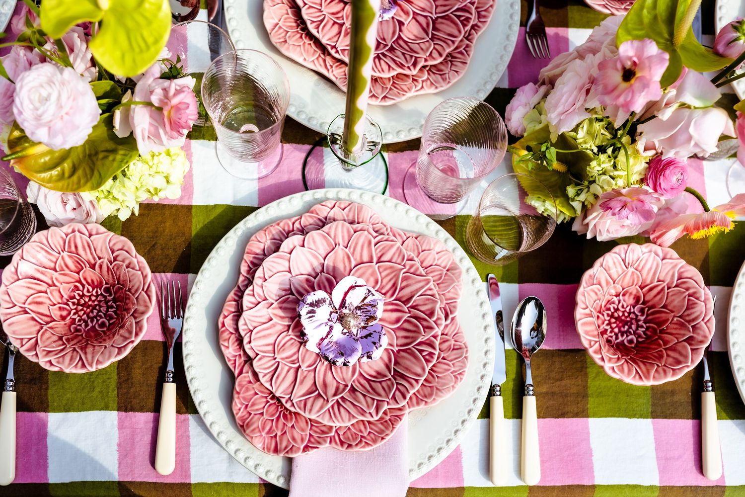Elegant pink floral ceramic plates and bowls on a pink and green plaid tablecloth with fresh flower arrangements.