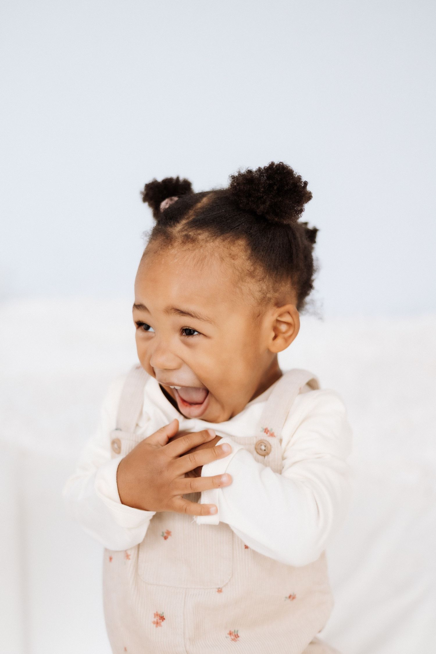 A laughing child in a white outfit lies on a light background showing pure joy and playful expressions.Shepperton Surrey photography studio