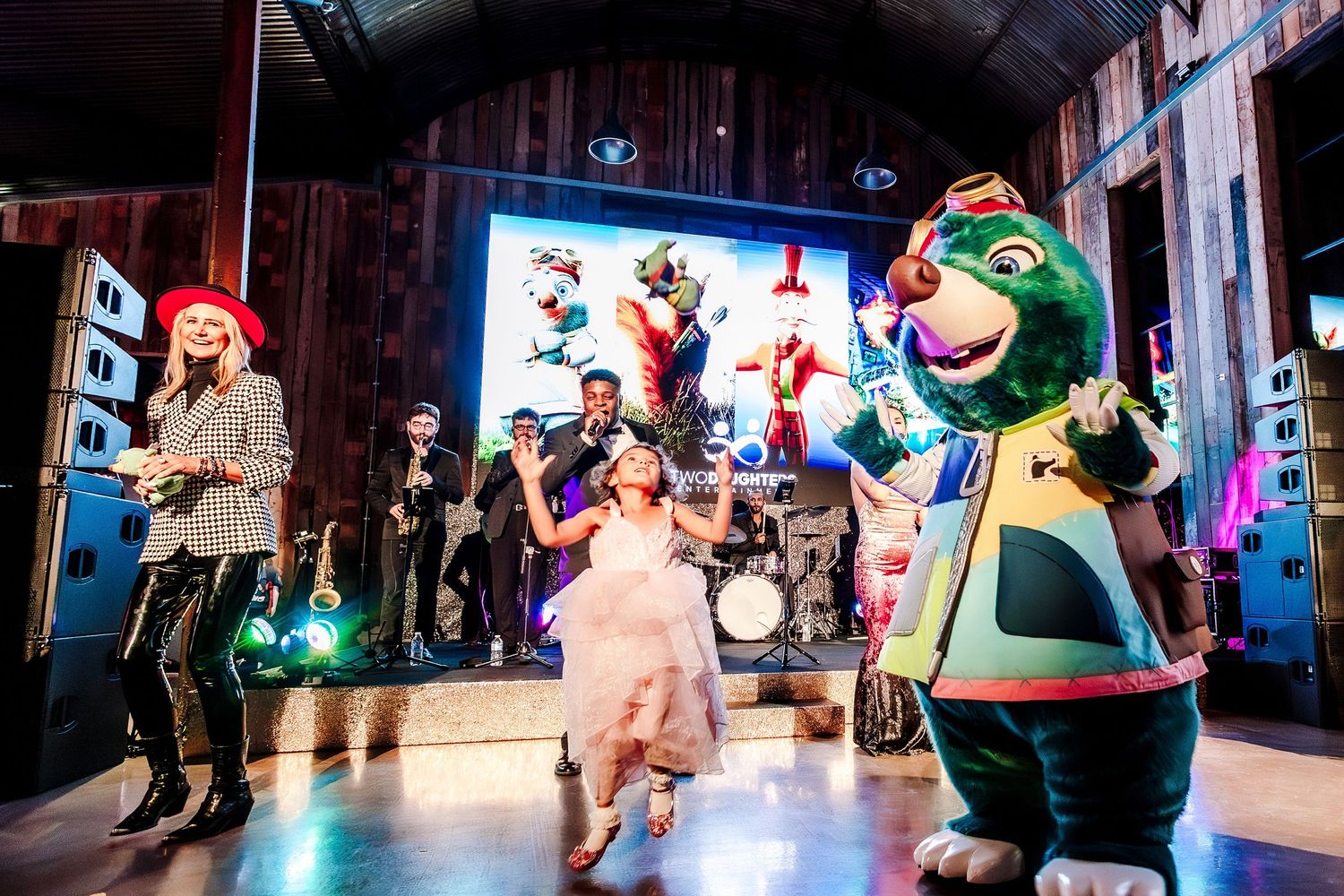 Children and mascots perform on a colorful stage with musicians at a lively kids entertainment show.