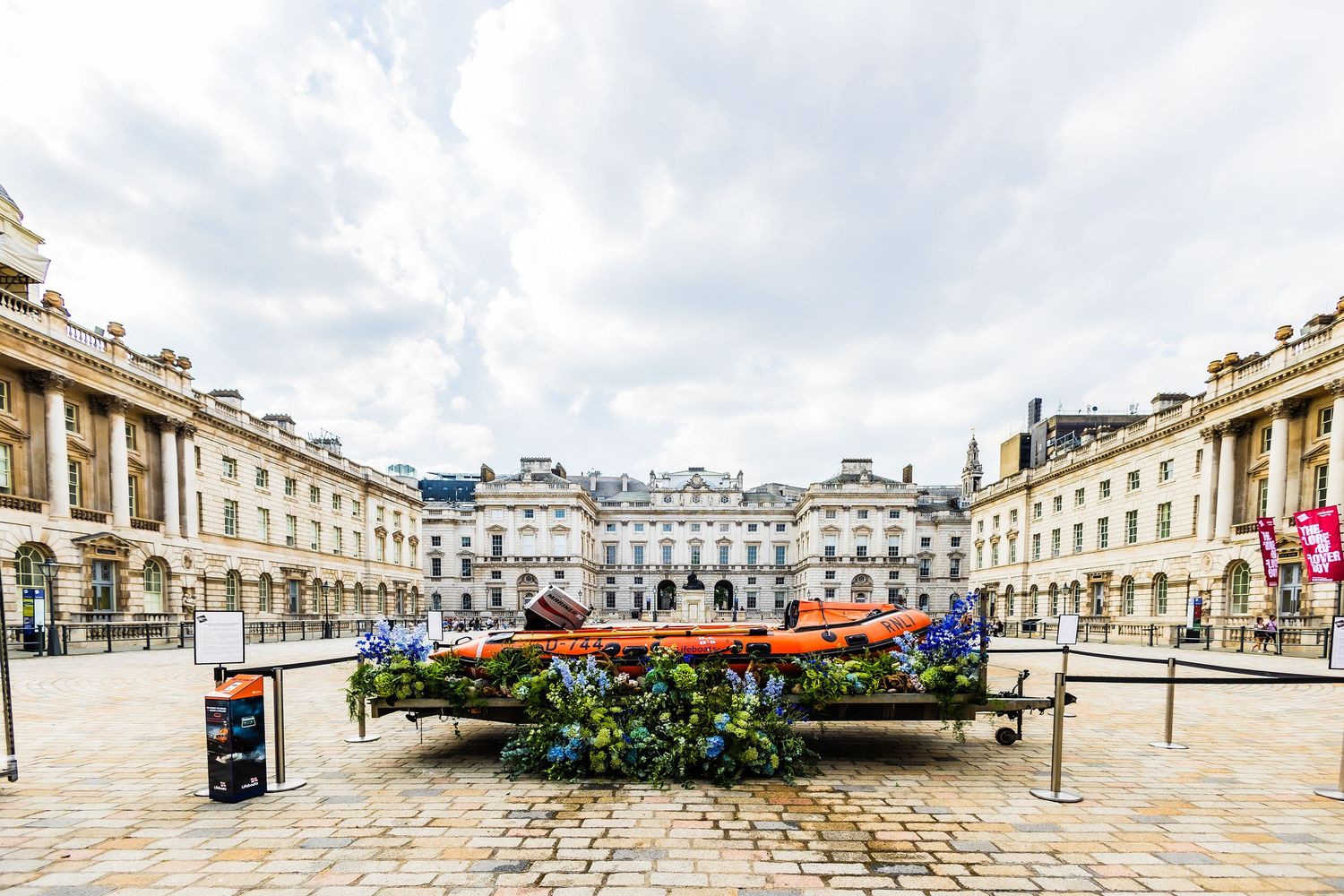 Somerset House courtyard with colorful flower displays on cobblestone plaza, surrounded by neoclassical architecture in London.