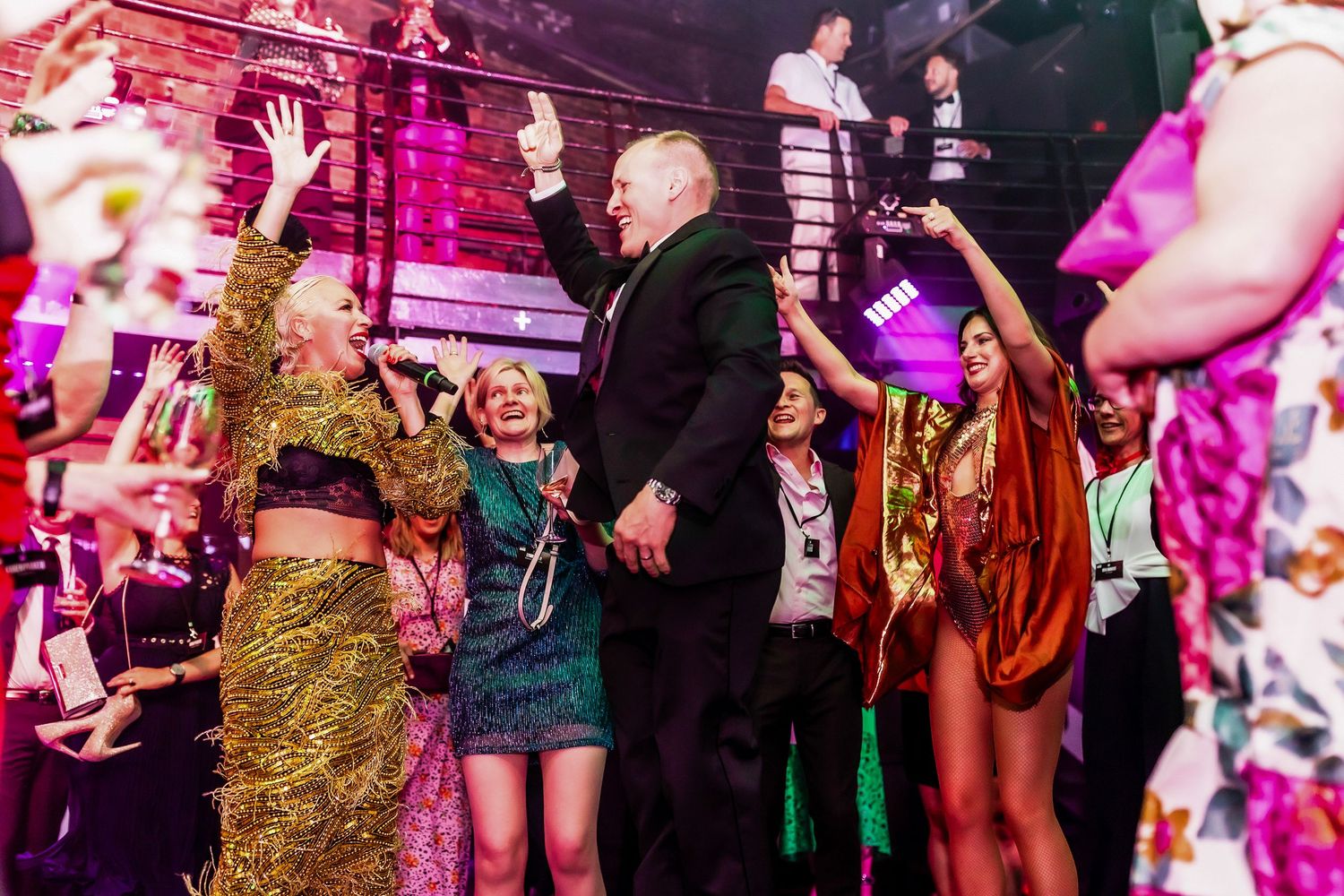 Colorful party crowd dancing and celebrating at a vibrant nightclub event with festive outfits and raised drinks.