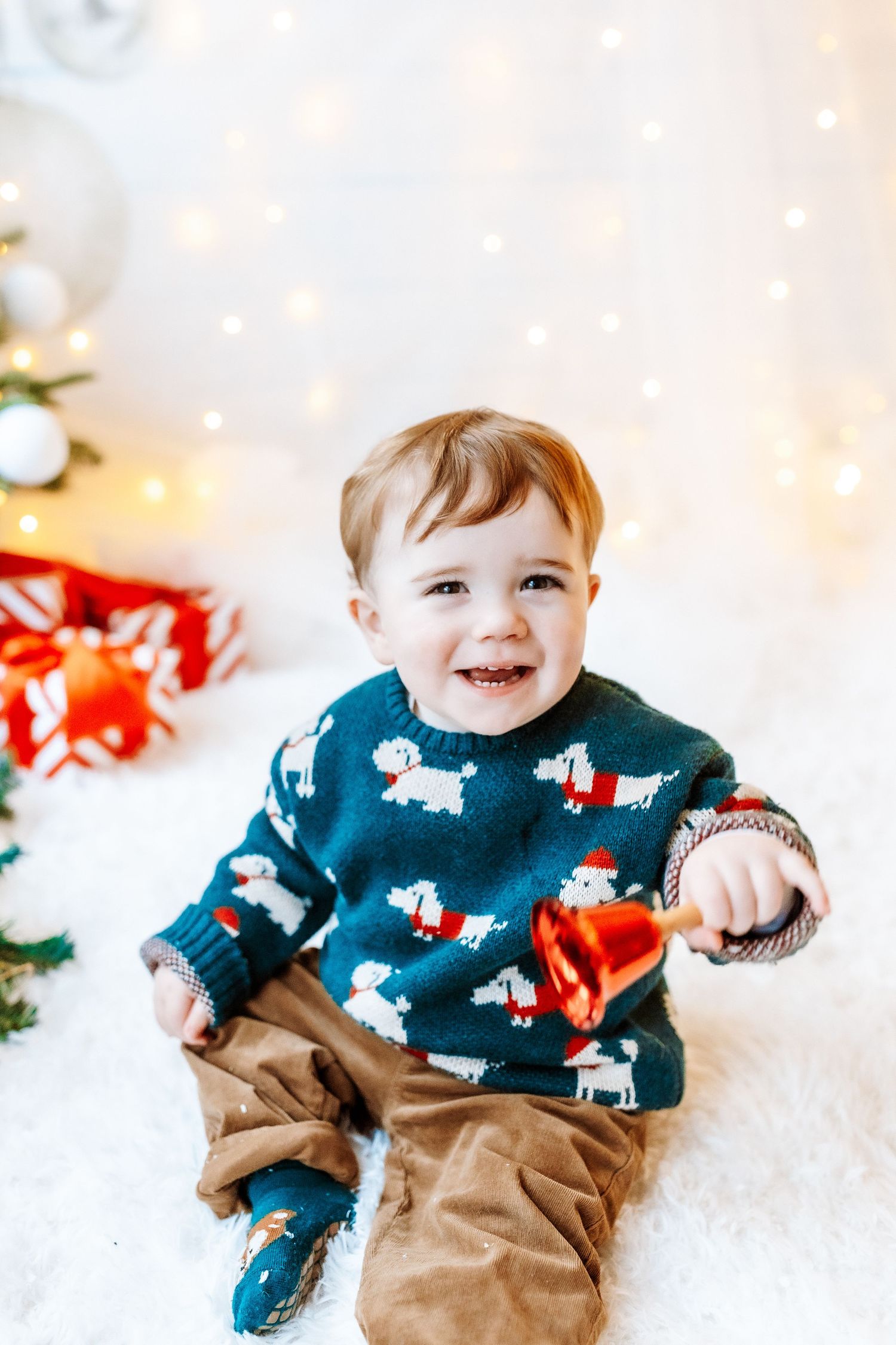 A child wearing a festive blue sweater with reindeer pattern sits in artificial snow during a holiday photoshoot.