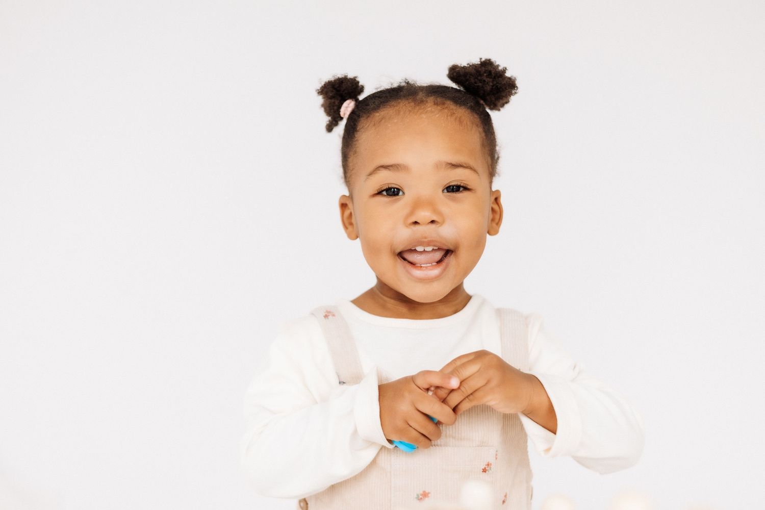 Toddler with hair buns wearing a white top smiles joyfully while playing. Shepperton Surrey photography studio portrait baby session