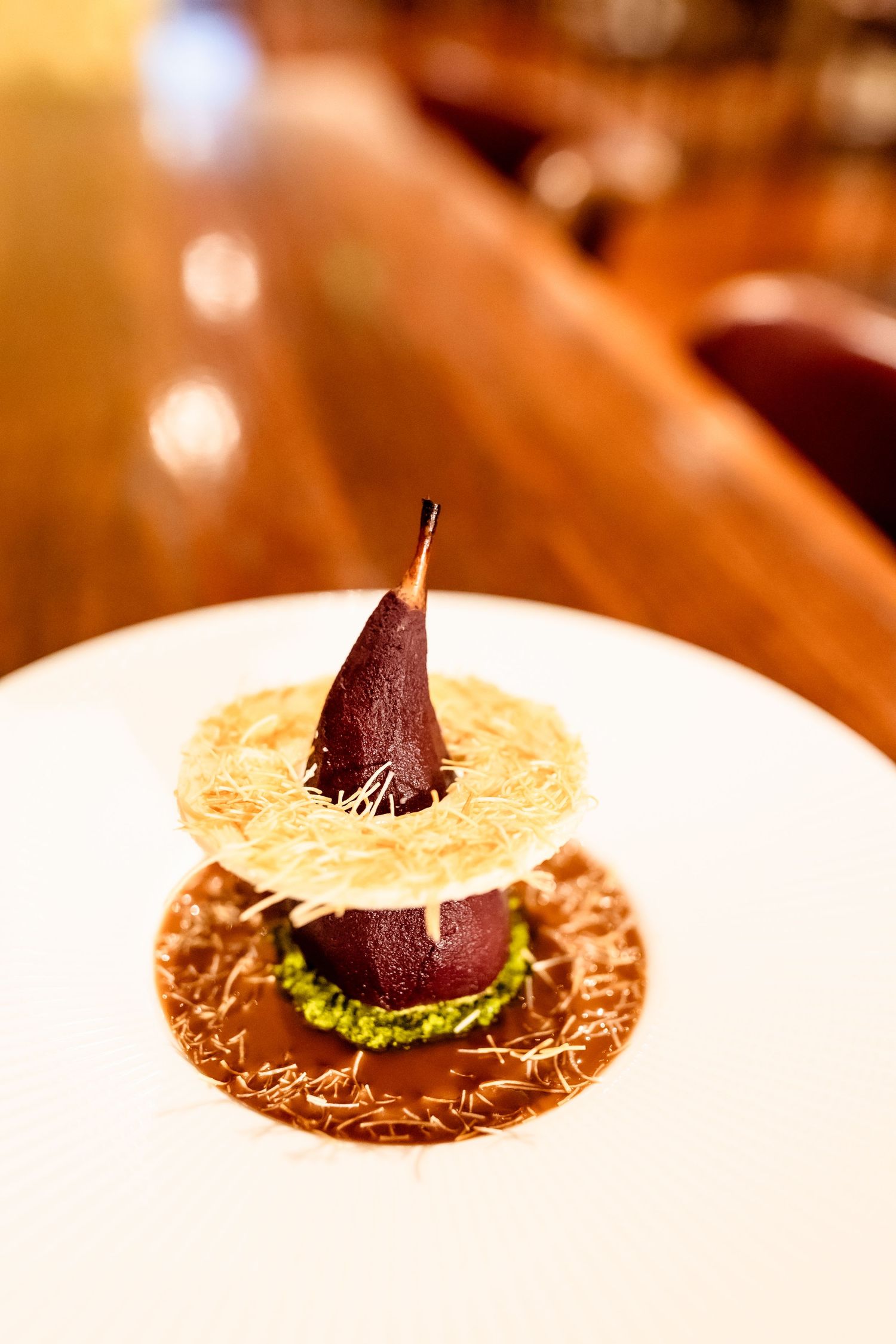 Elegant poached pear dessert on a white plate with pistachio cream and crispy tuile in a fine dining restaurant.