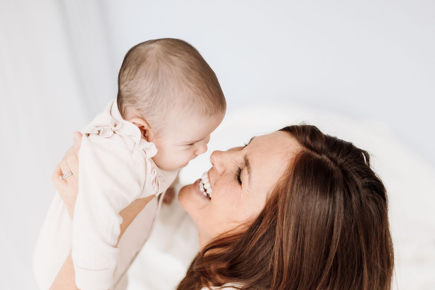 Parent and baby laughing together against a minimalist white background. candid photography baby, family Shepperton Surrey studio