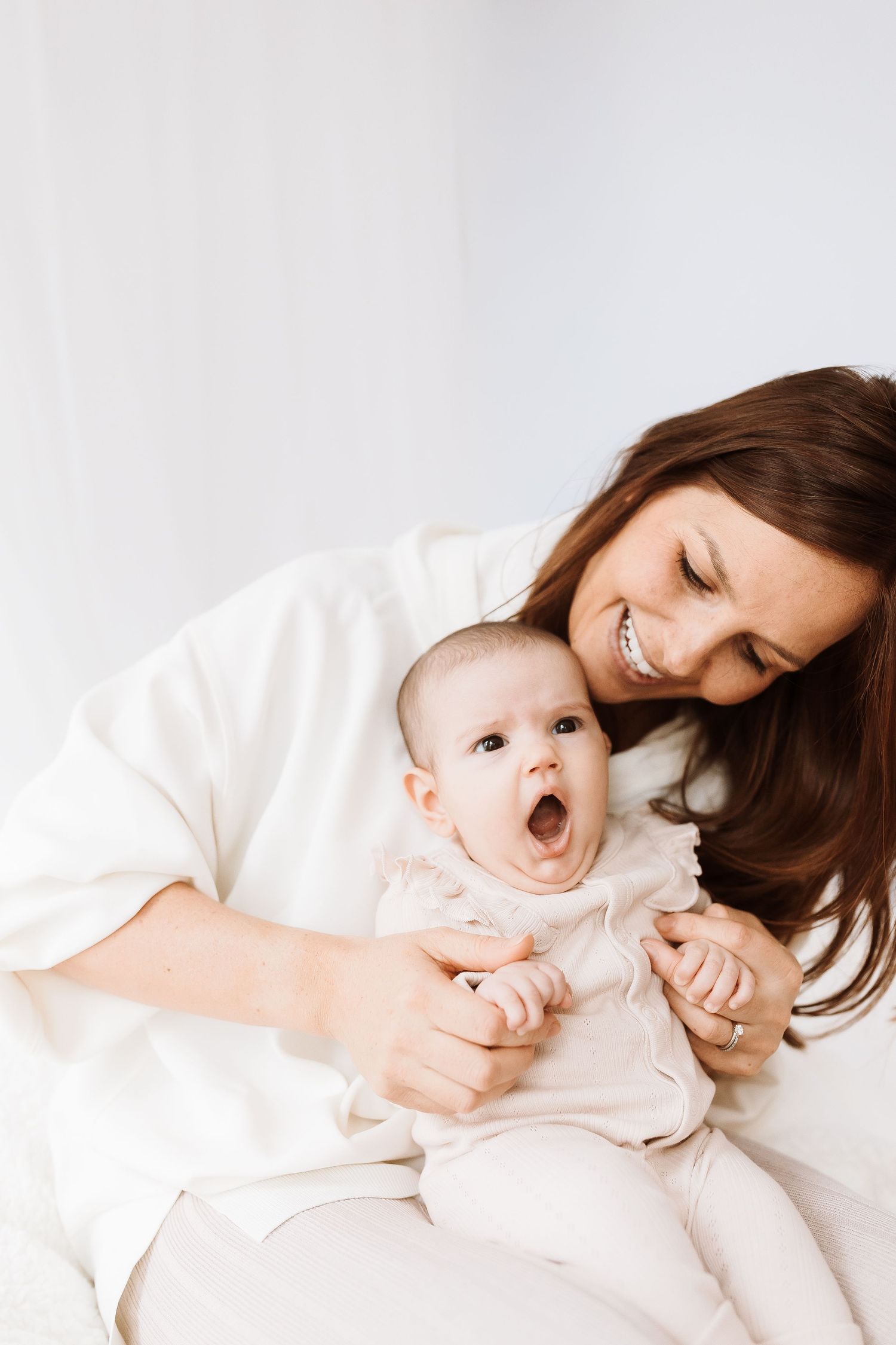 Parent and baby laughing together against a minimalist white background. candid photography baby, family Shepperton Surrey studio